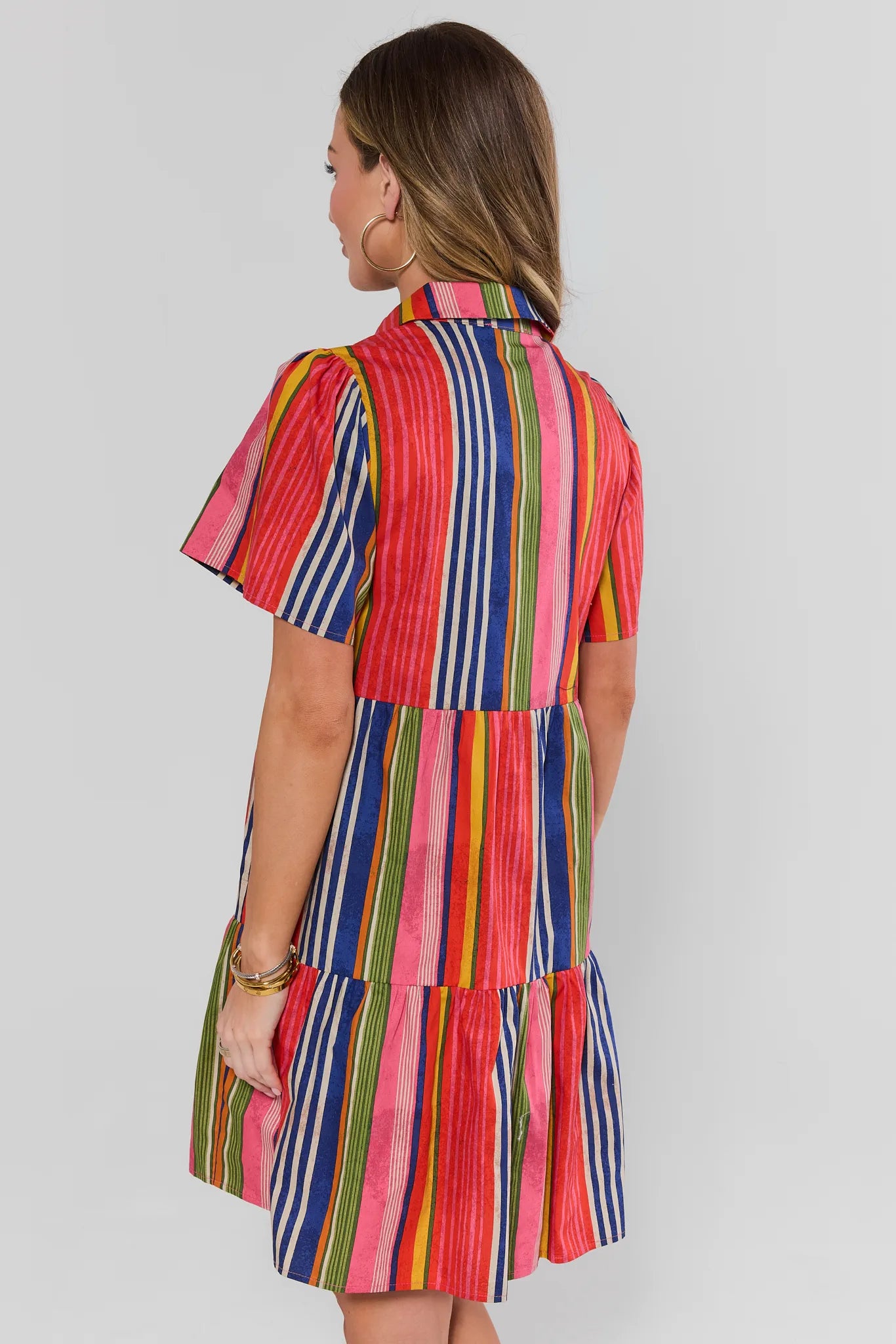 Woman wearing a colorful striped dress on a plain background stand