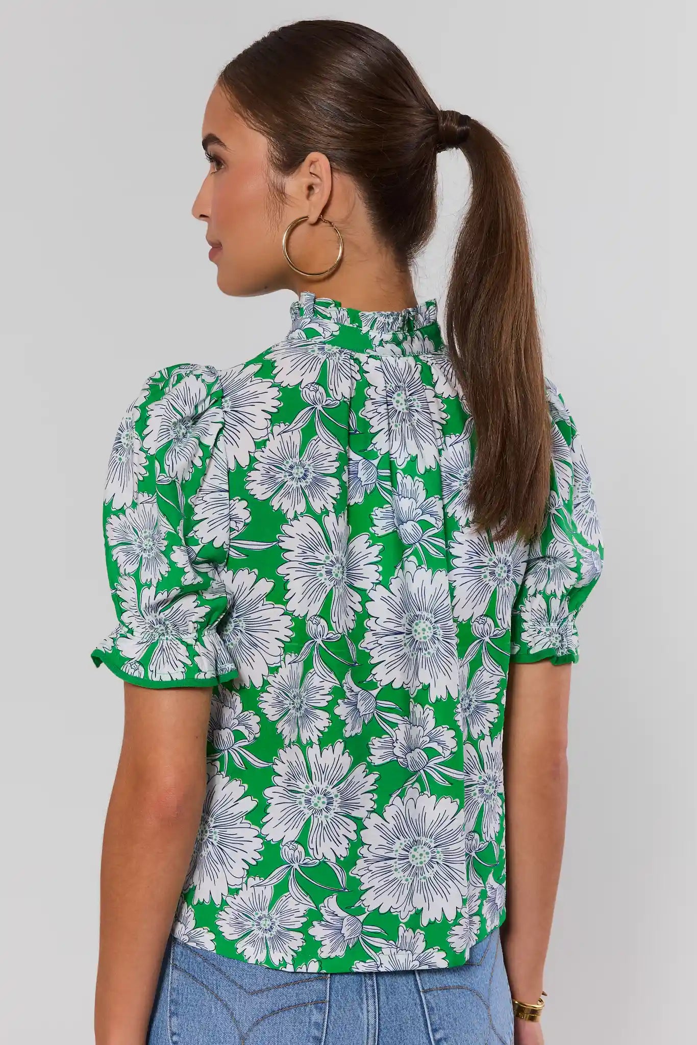 Woman wearing a green floral blouse against a plain background stand