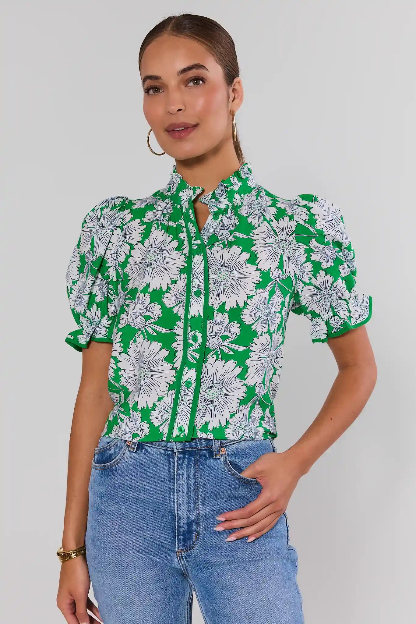 Woman wearing a green floral blouse and blue jeans against a white background