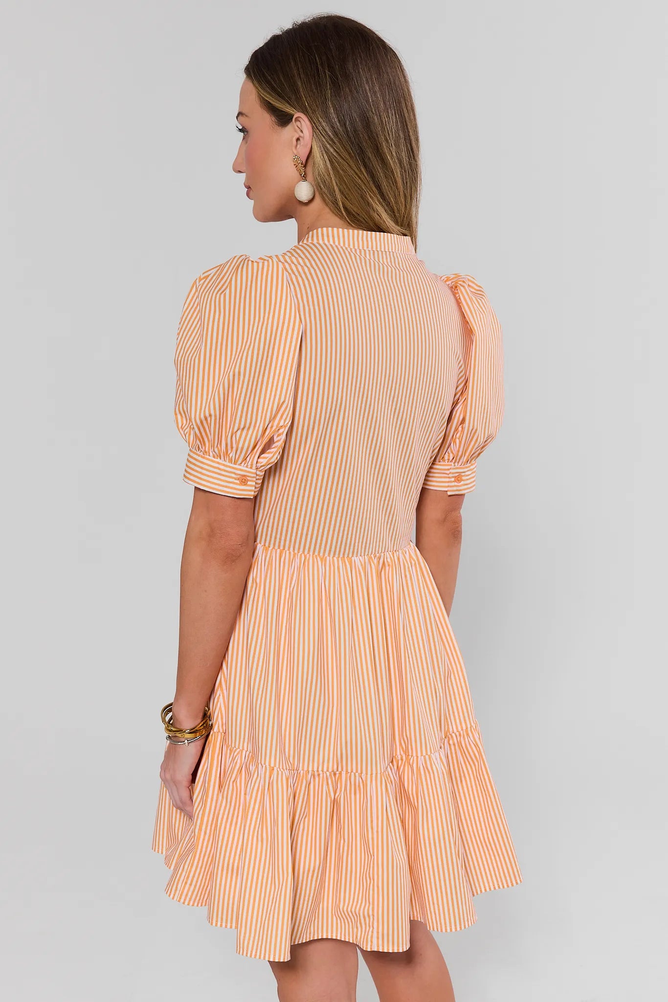 Woman wearing a peach and white striped dress on a gray background back