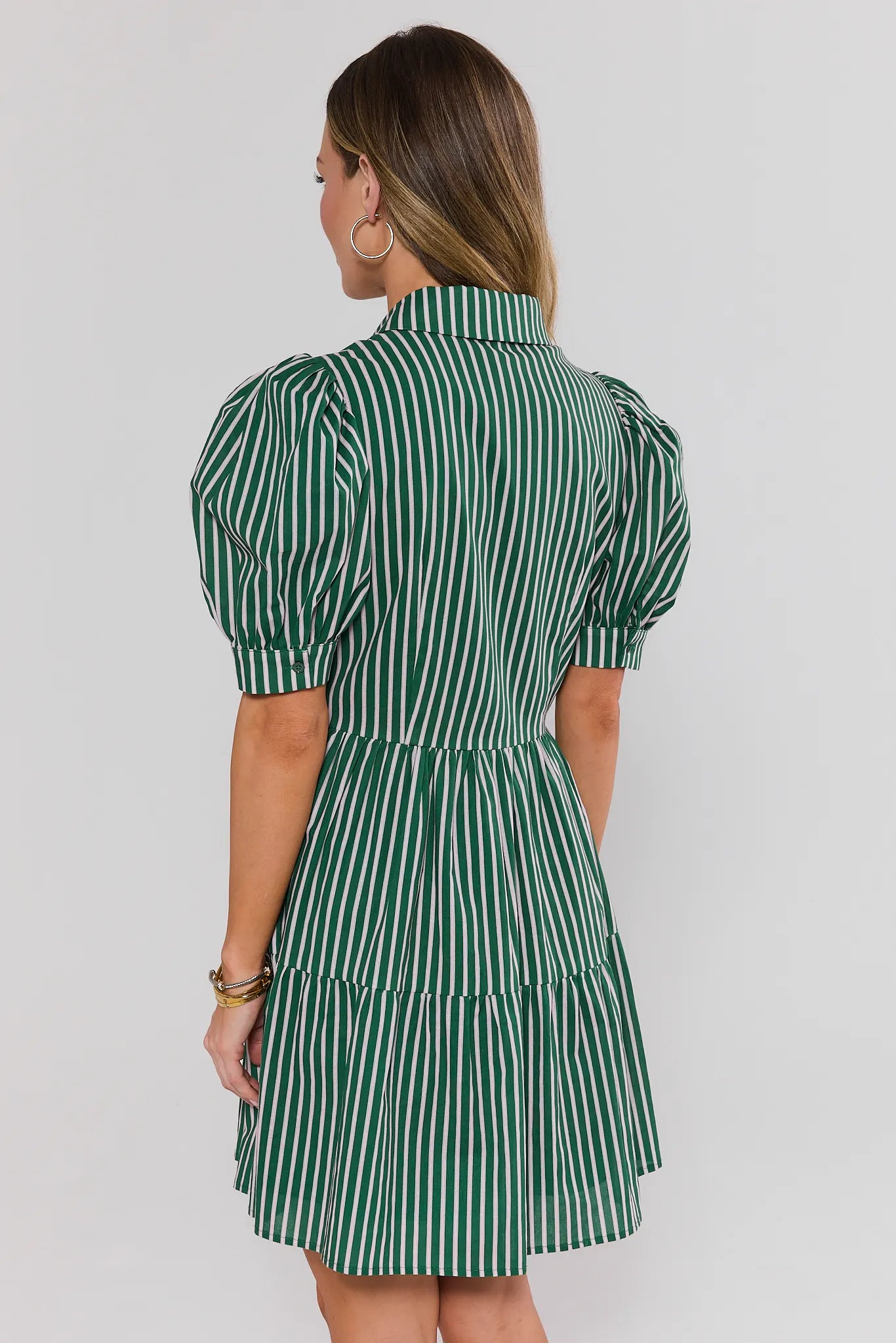Woman wearing a green and white striped dress against a plain background stand