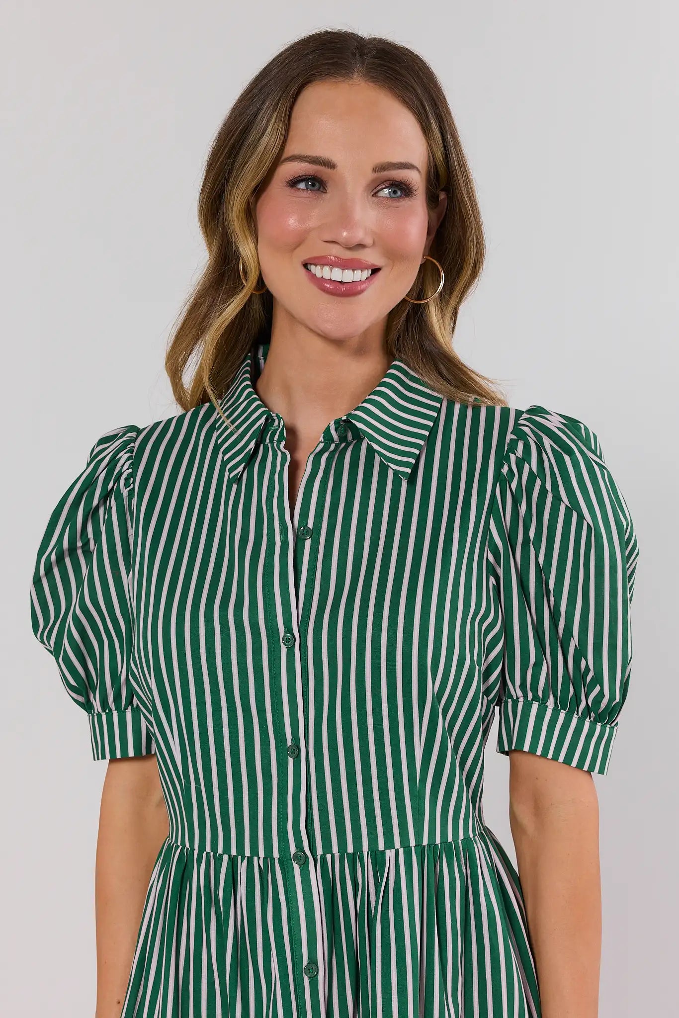 Woman wearing a green and white striped dress against a plain background close up