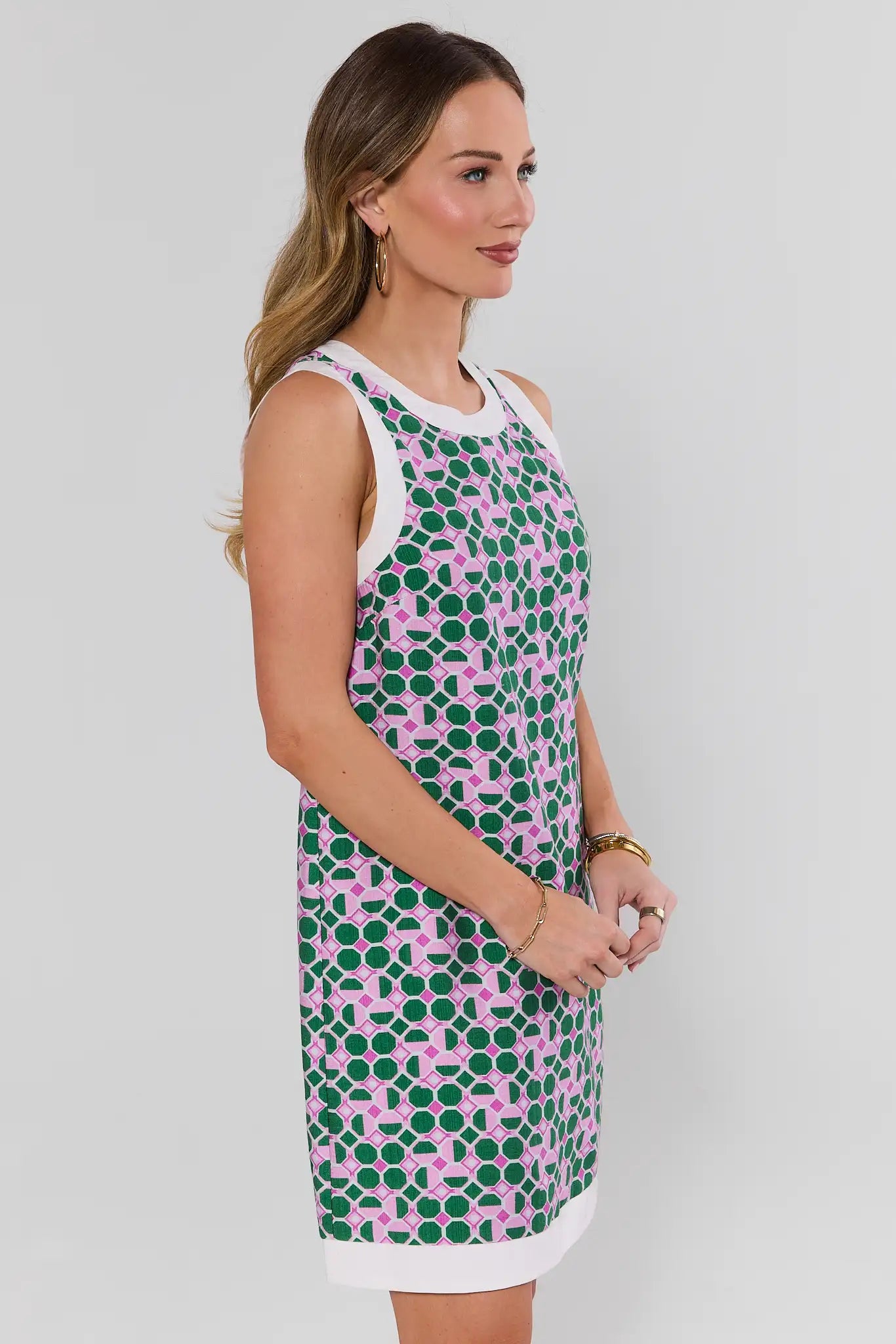Woman wearing a sleeveless dress with pink and green pattern on a plain background side