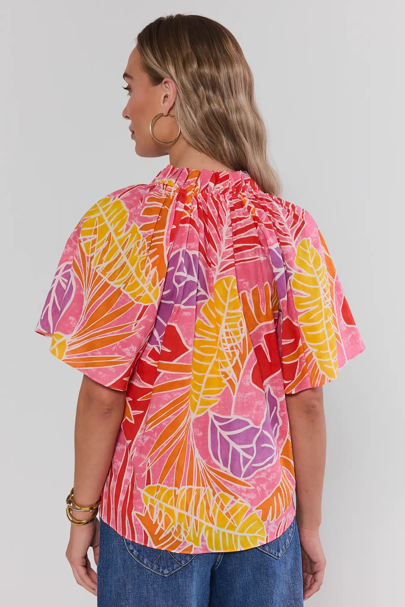 Woman standing wearing a colorful tropical leaf patterned blouse against a plain background