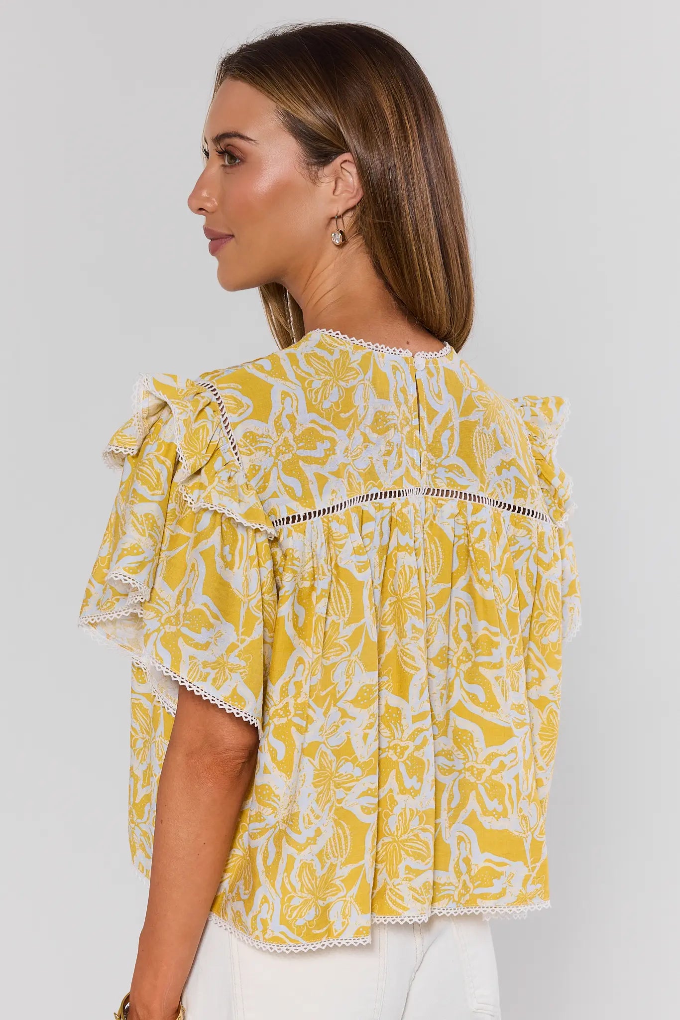 Woman wearing a yellow floral blouse against a white background standing