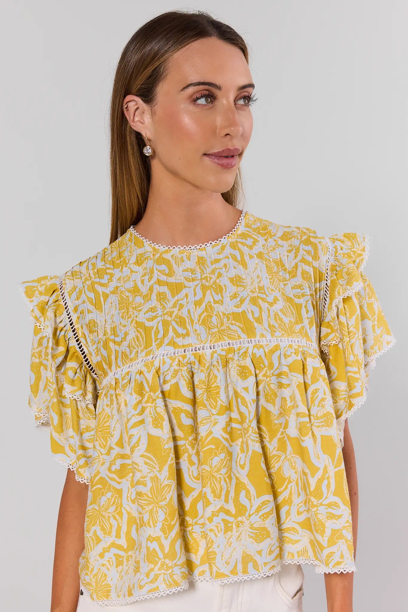 Woman wearing a yellow floral blouse against a plain background
