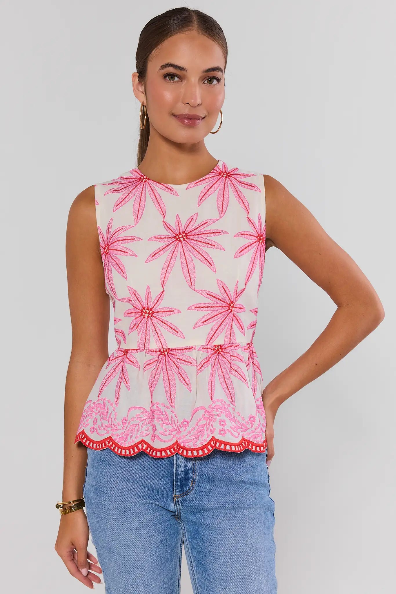Woman wearing a sleeveless top with pink floral pattern and blue jeans on a white background