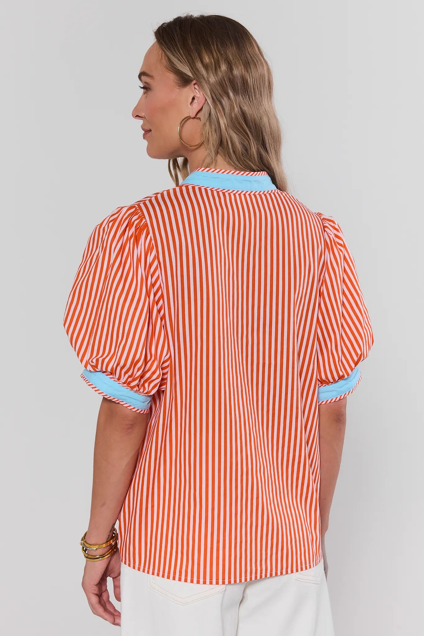 Woman standing wearing a red and white striped shirt with blue trim on a plain background
