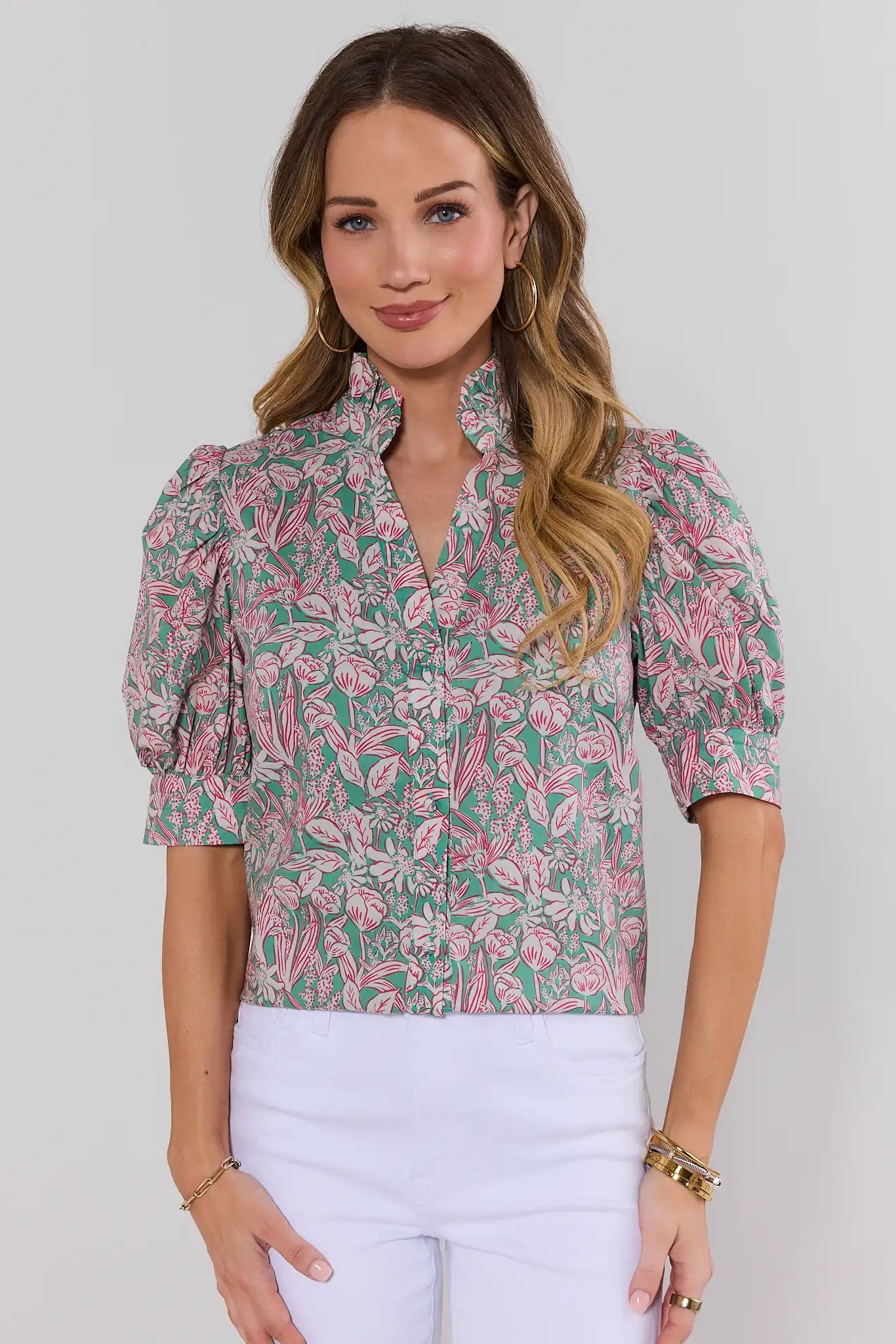 Woman wearing a pink and green floral blouse with white pants on a plain background