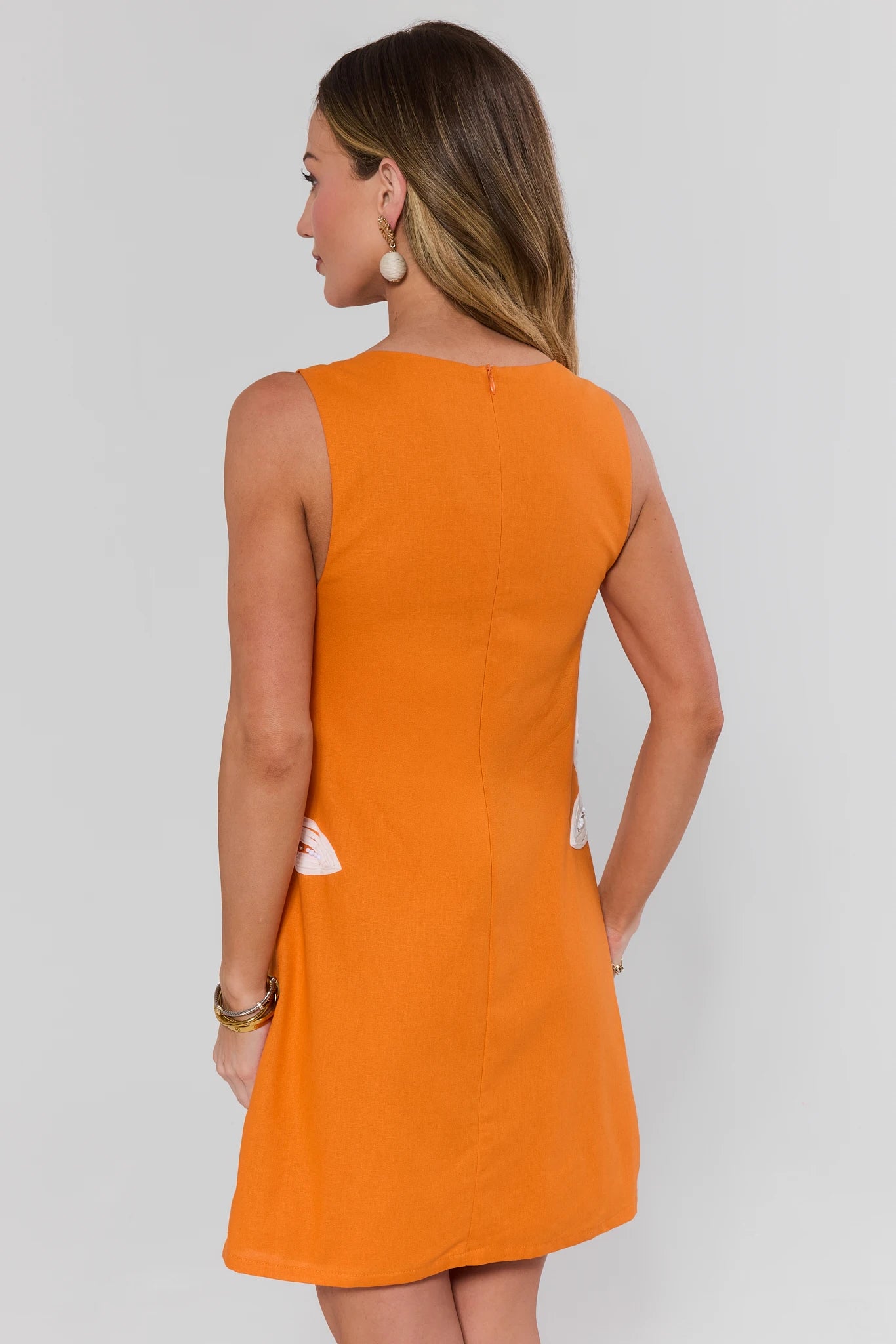 Woman wearing an orange dress against a white background standing