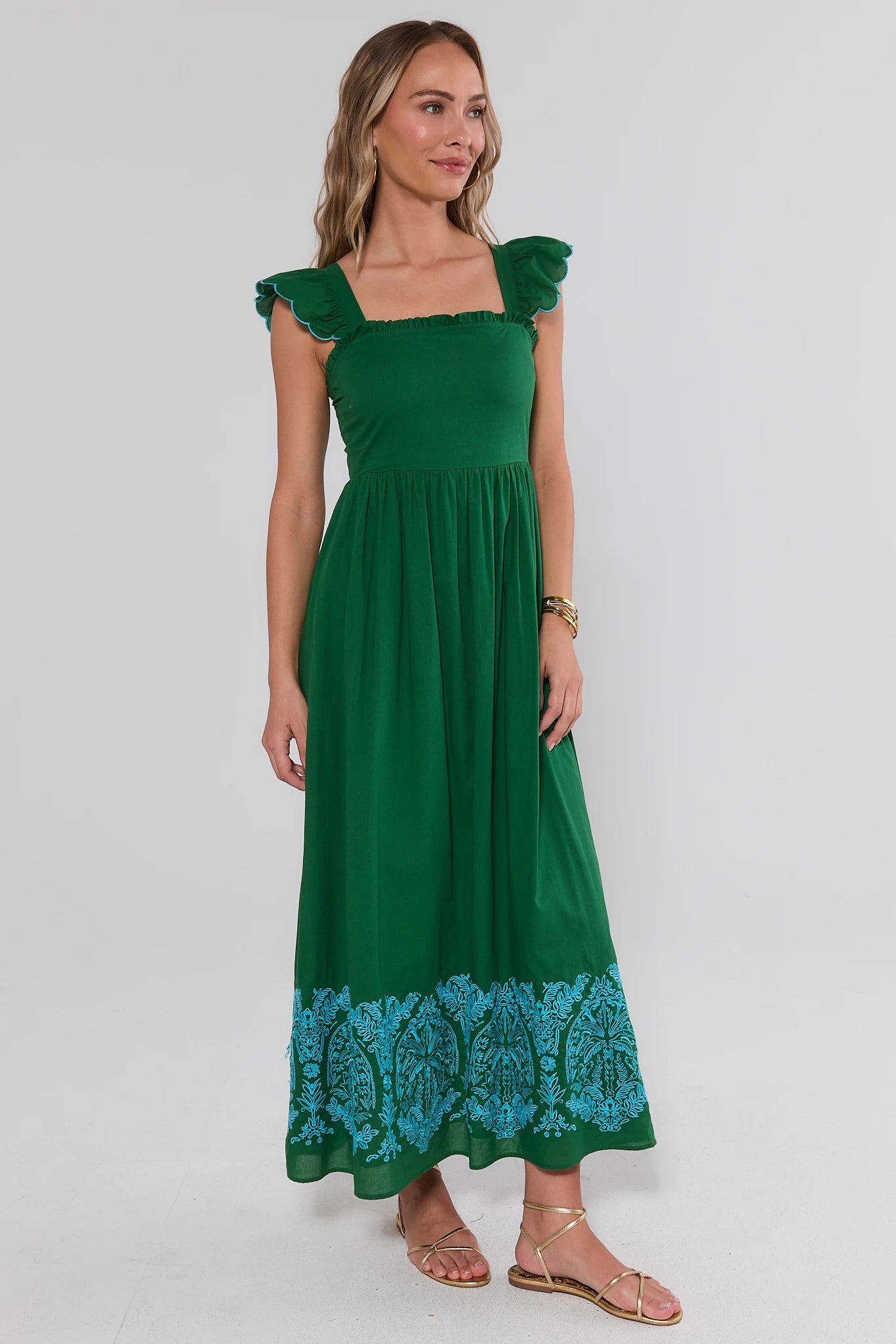 Woman wearing a green dress with blue lace trim on a white background side