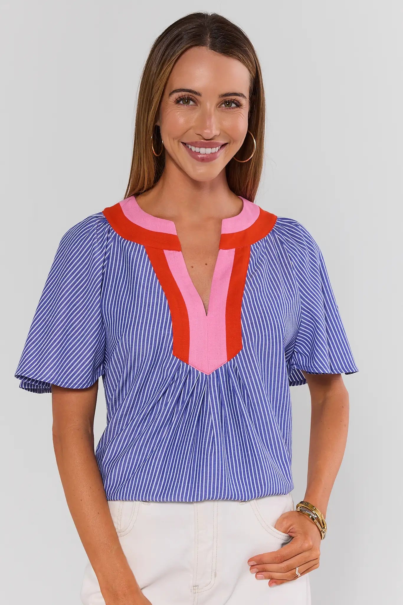 Woman wearing a blue and red striped blouse with a white background standing