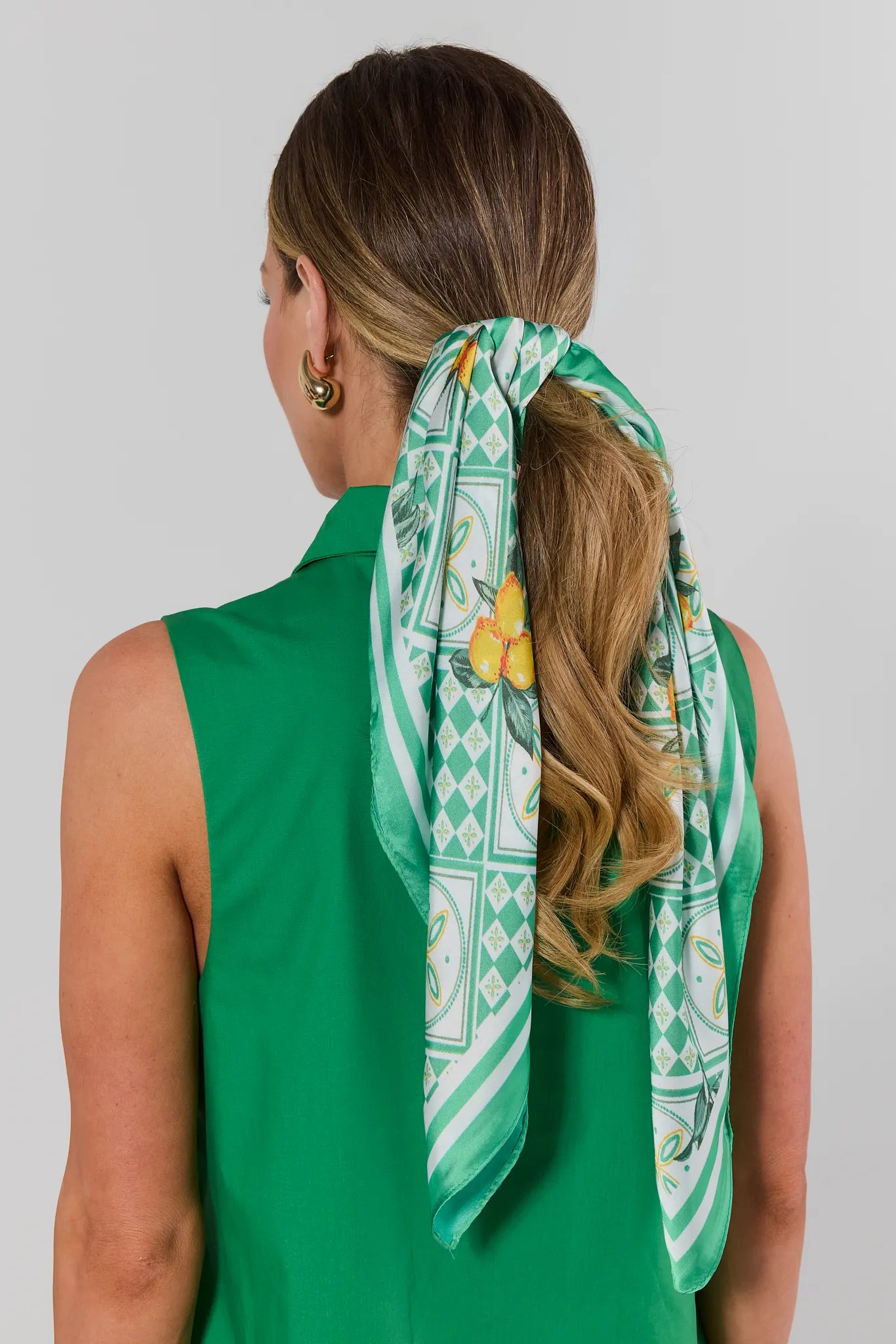 Woman wearing a green patterned scarf in her hair against a plain background