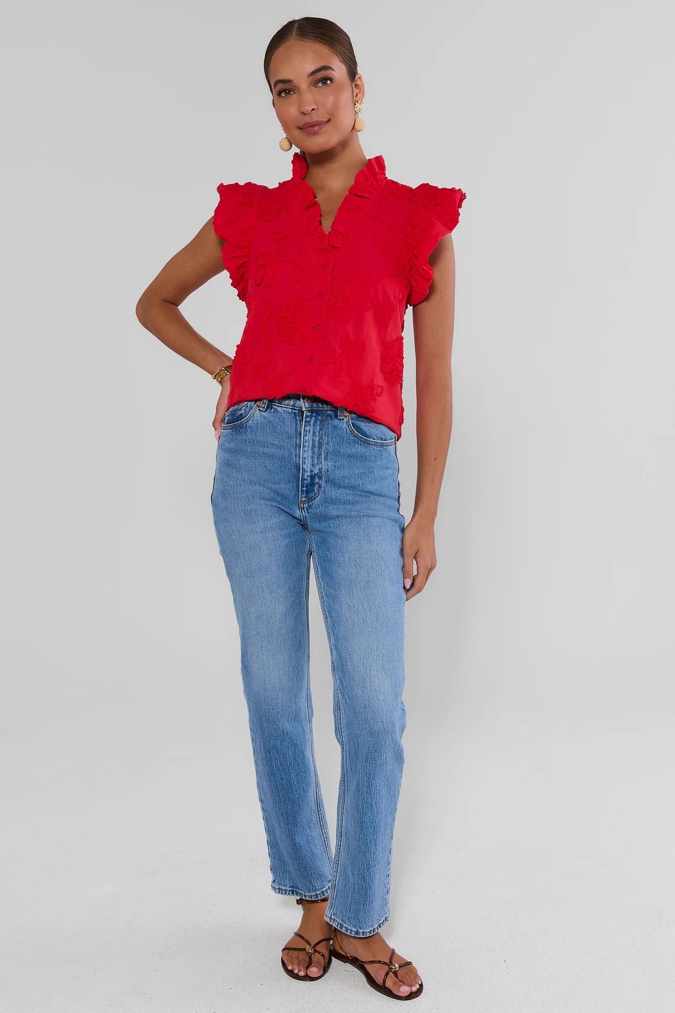 Woman wearing a red blouse with ruffled sleeves and blue jeans on a gray background