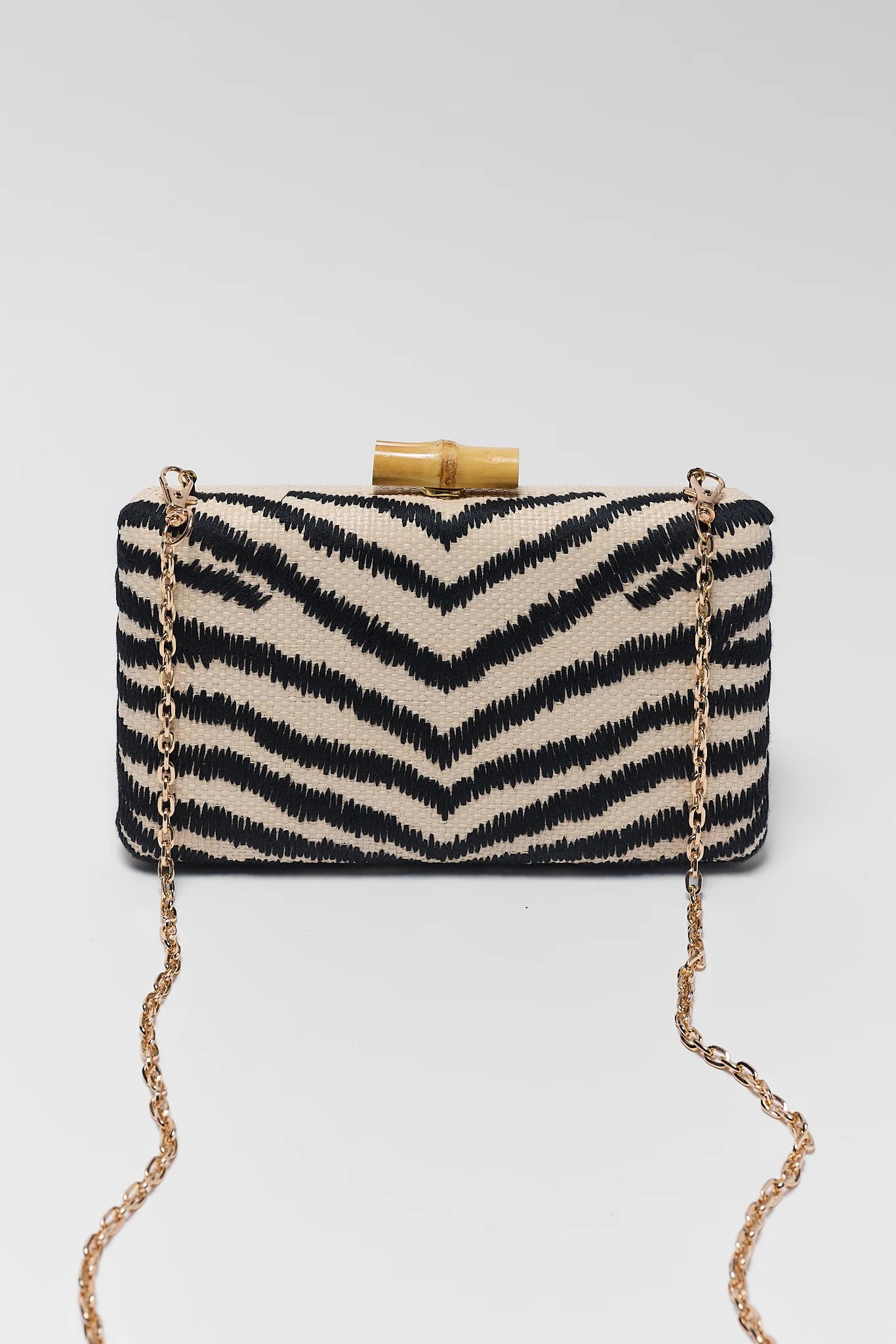 Black and white zebra patterned clutch bag with gold chain on a white background