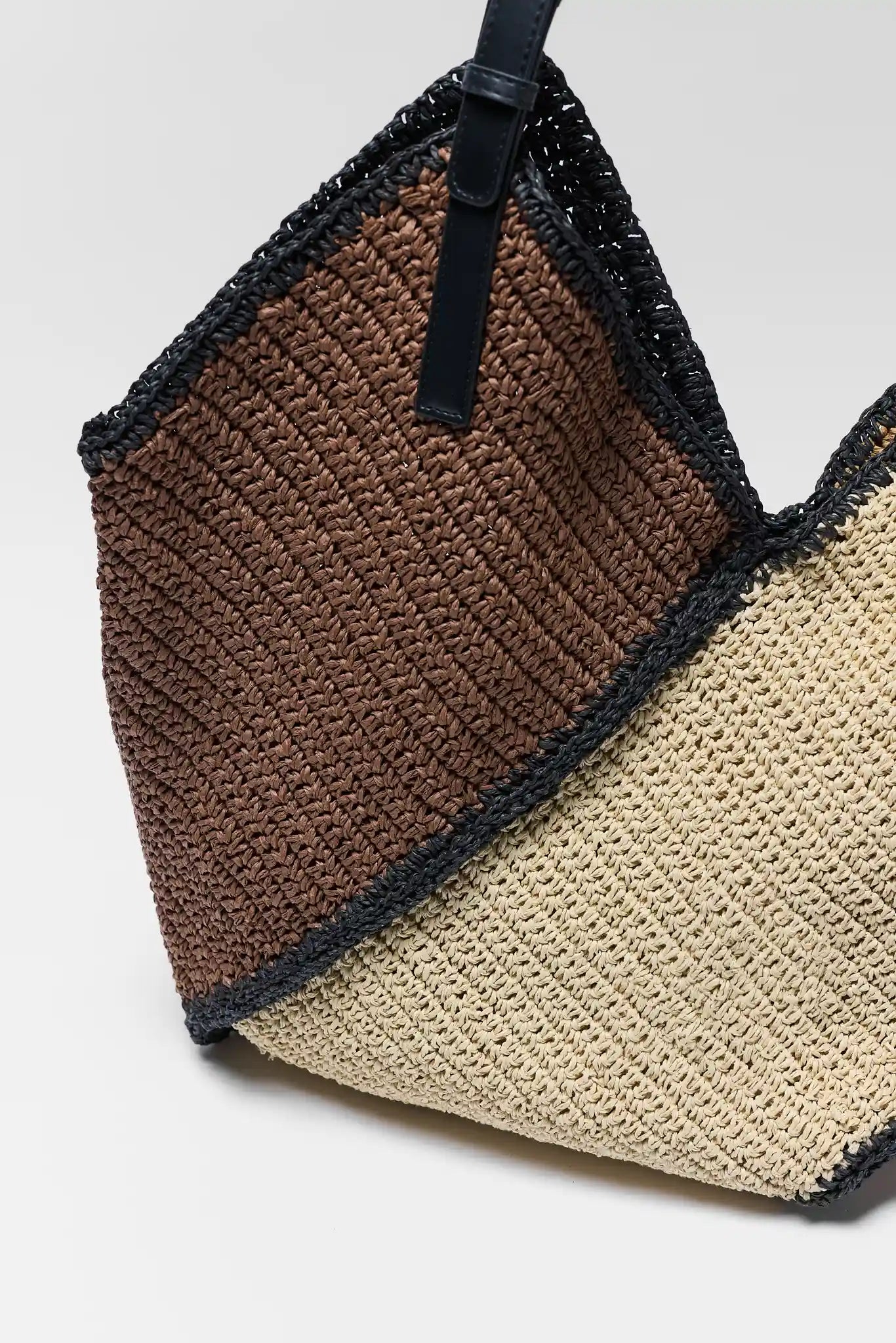 Crocheted bag with brown, black, and beige sections on a light gray background close up