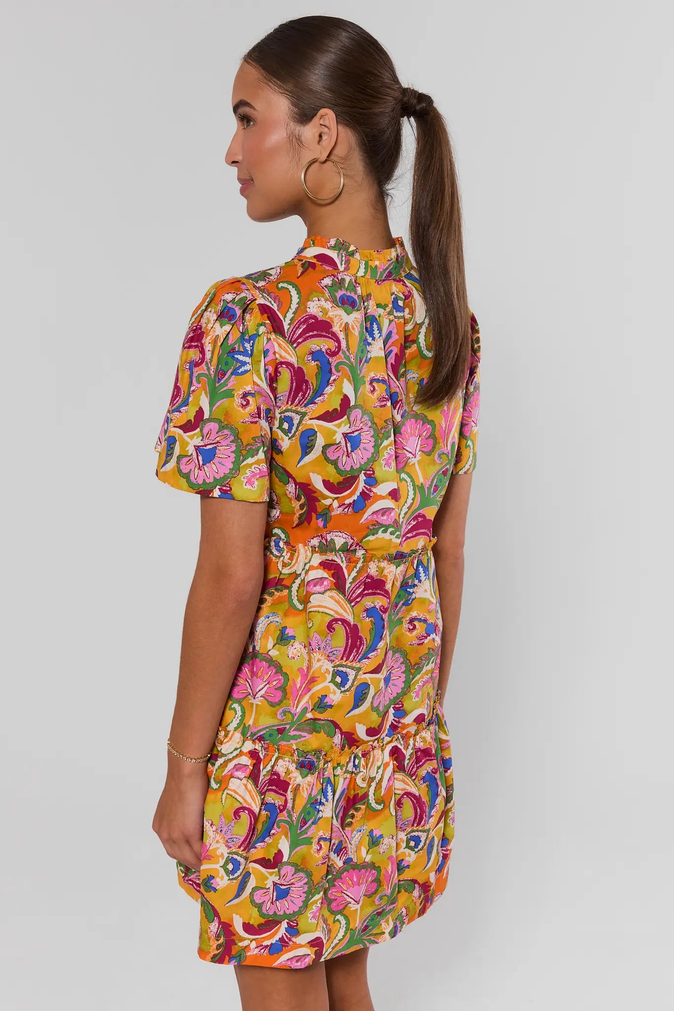 Woman standing wearing a colorful floral dress against a plain background