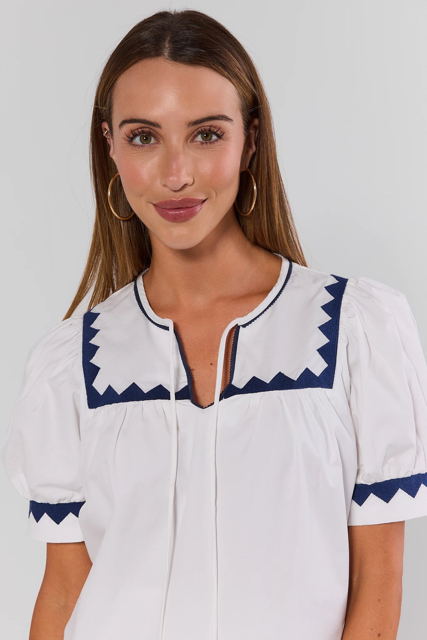 Woman wearing a white dress with blue accents on a plain background close up
