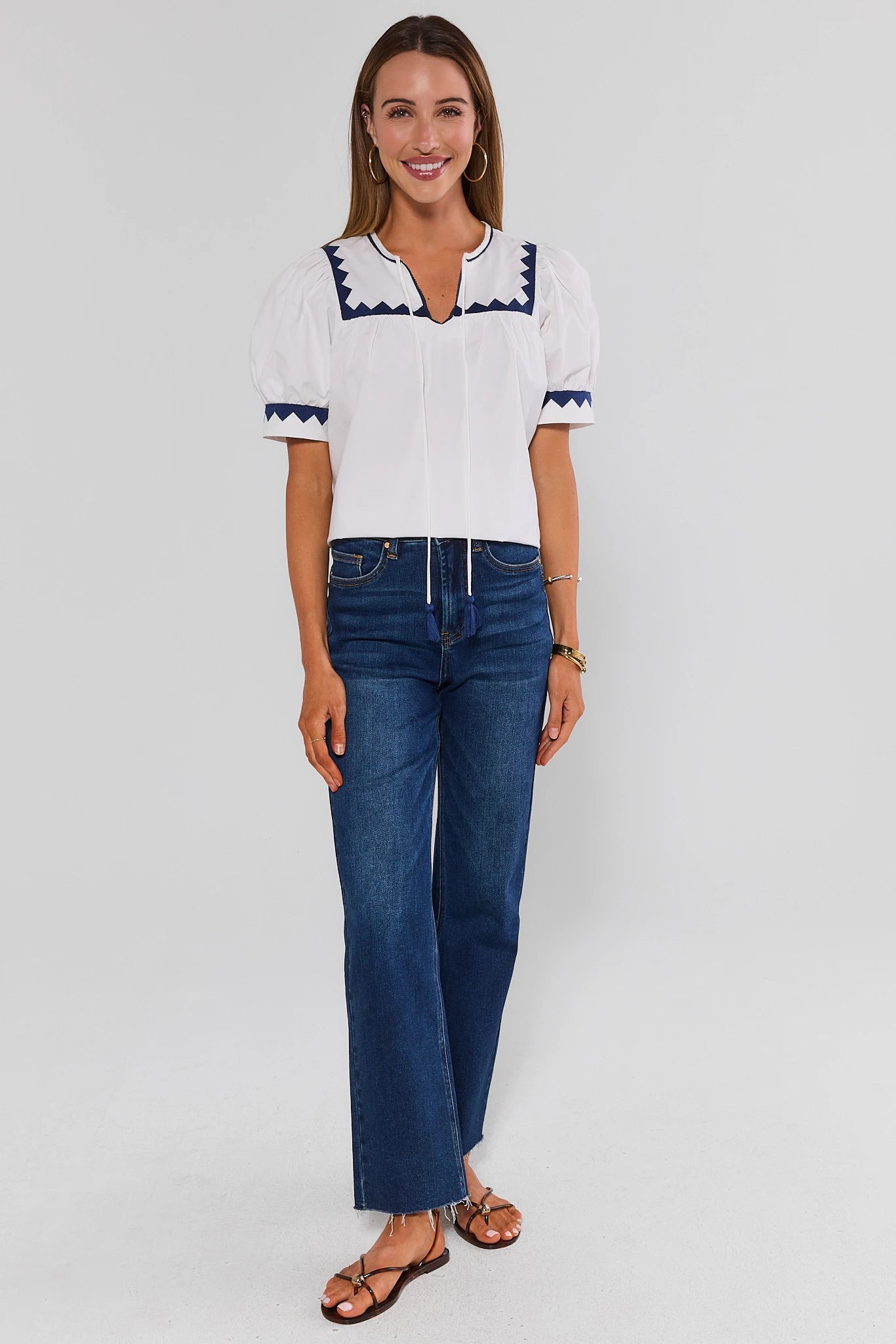 Woman wearing a white blouse with blue accents and blue jeans on a light gray background