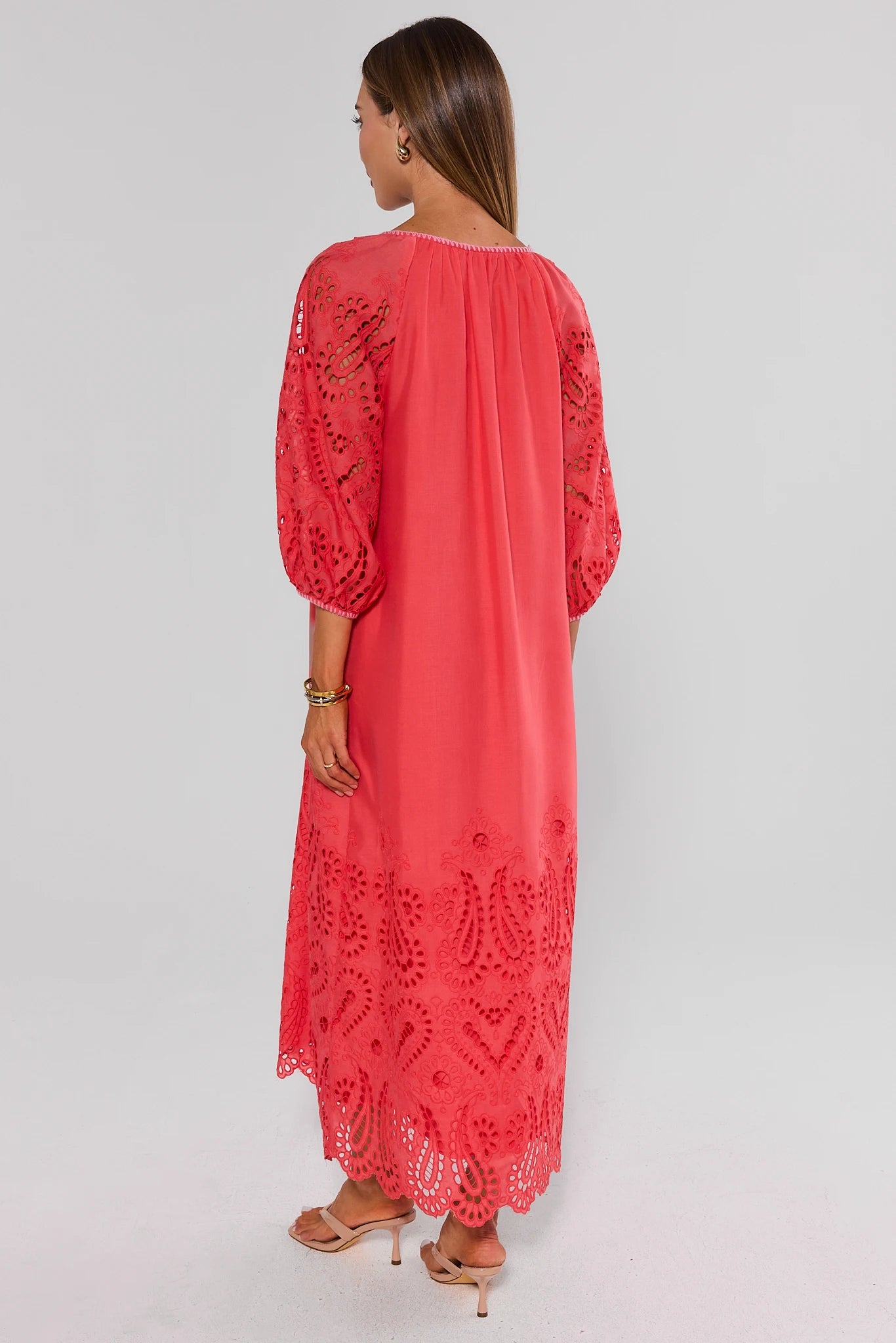 Woman walking wearing a coral dress with lace details on a plain background