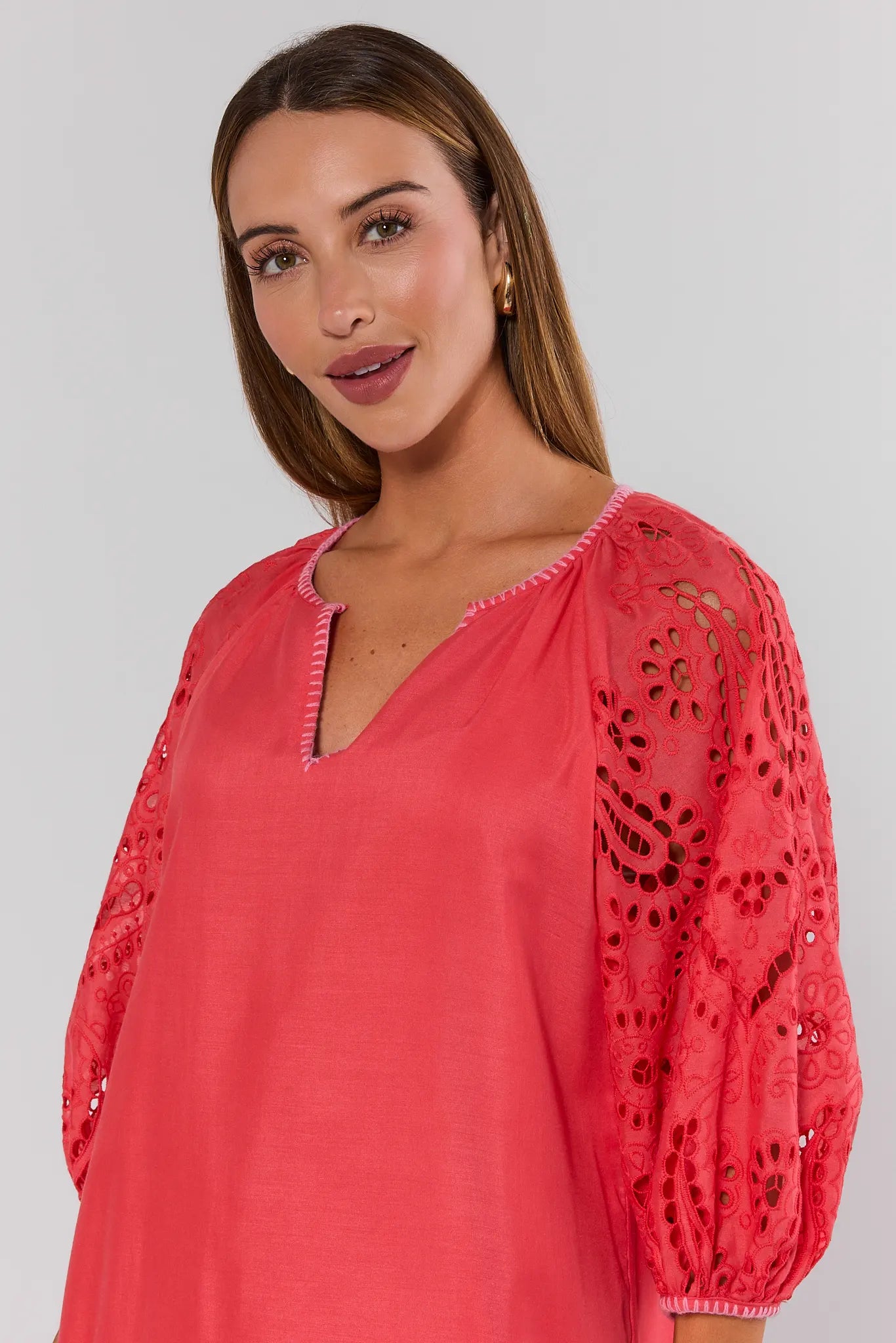 Woman wearing a coral pink dress with intricate lace sleeves on a plain background close up