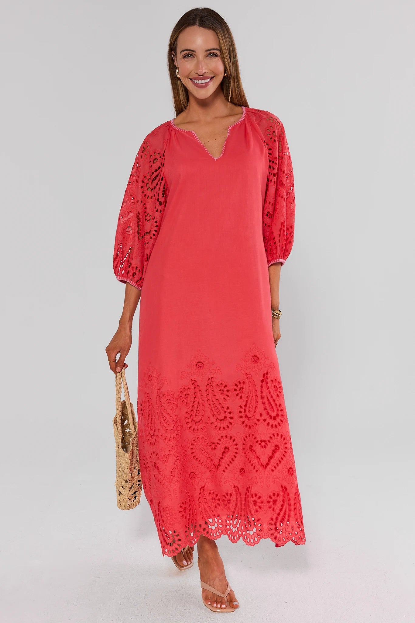 Woman wearing a coral dress with lace details on a plain background standing