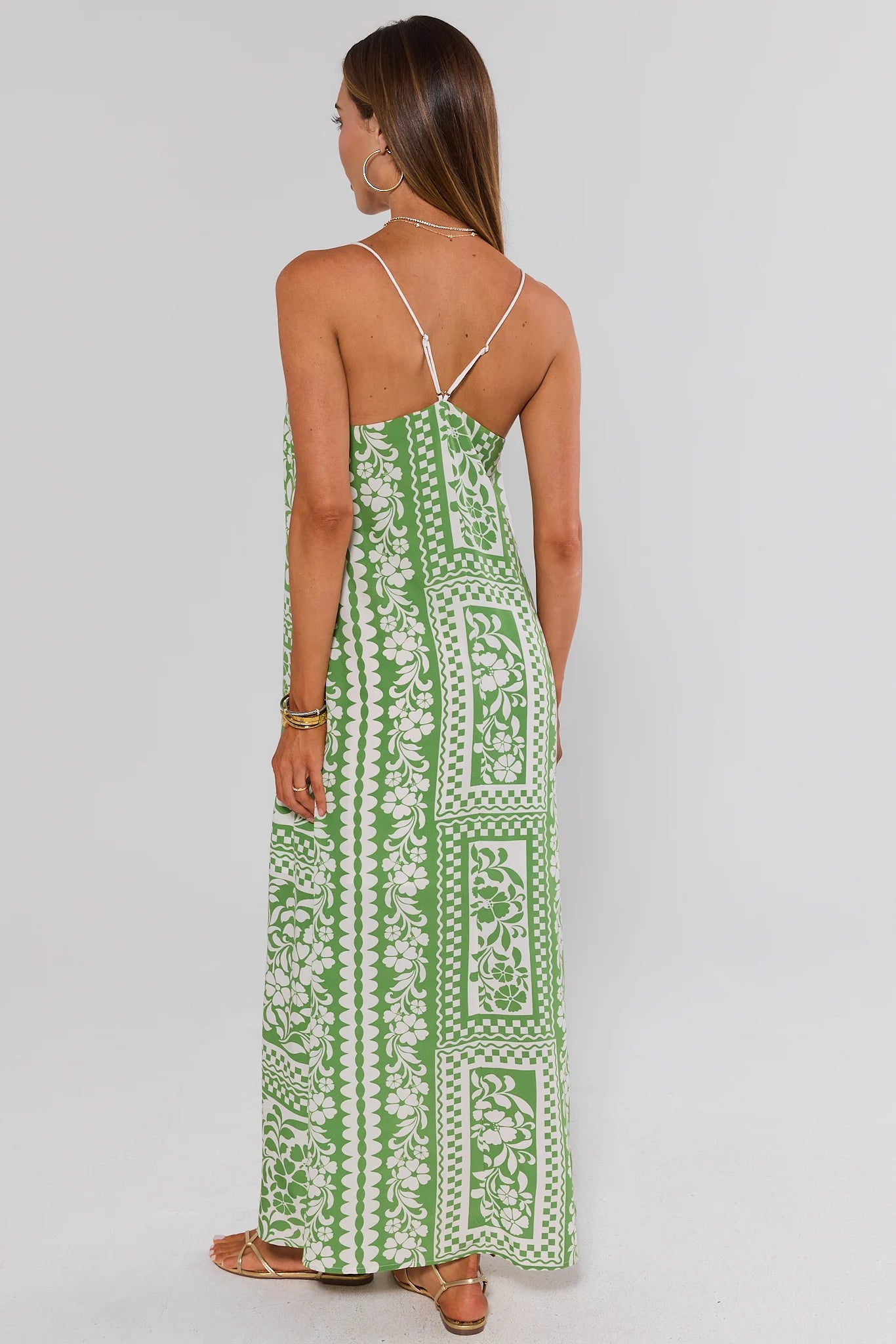 Woman wearing a green white patterned dress on a gray background standing