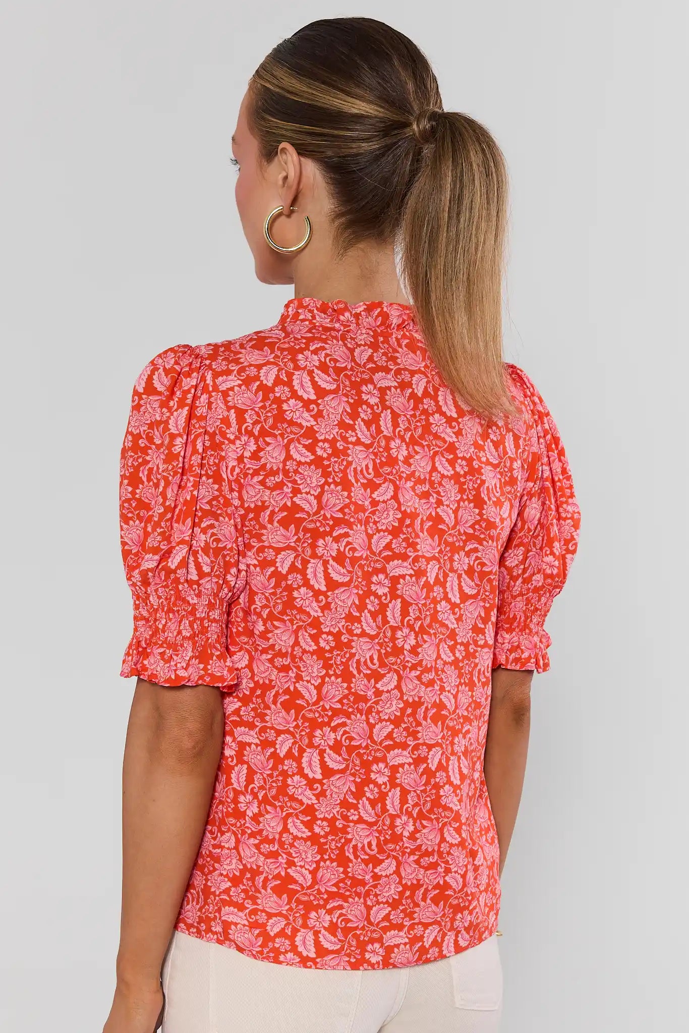 Woman standing wearing a red floral blouse against a plain background
