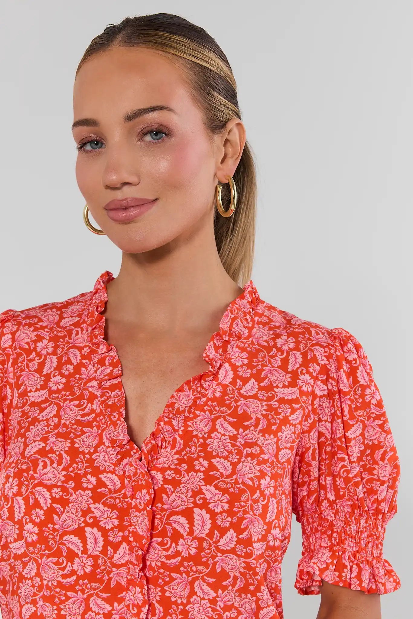 Woman wearing a red floral blouse against a plain background close up