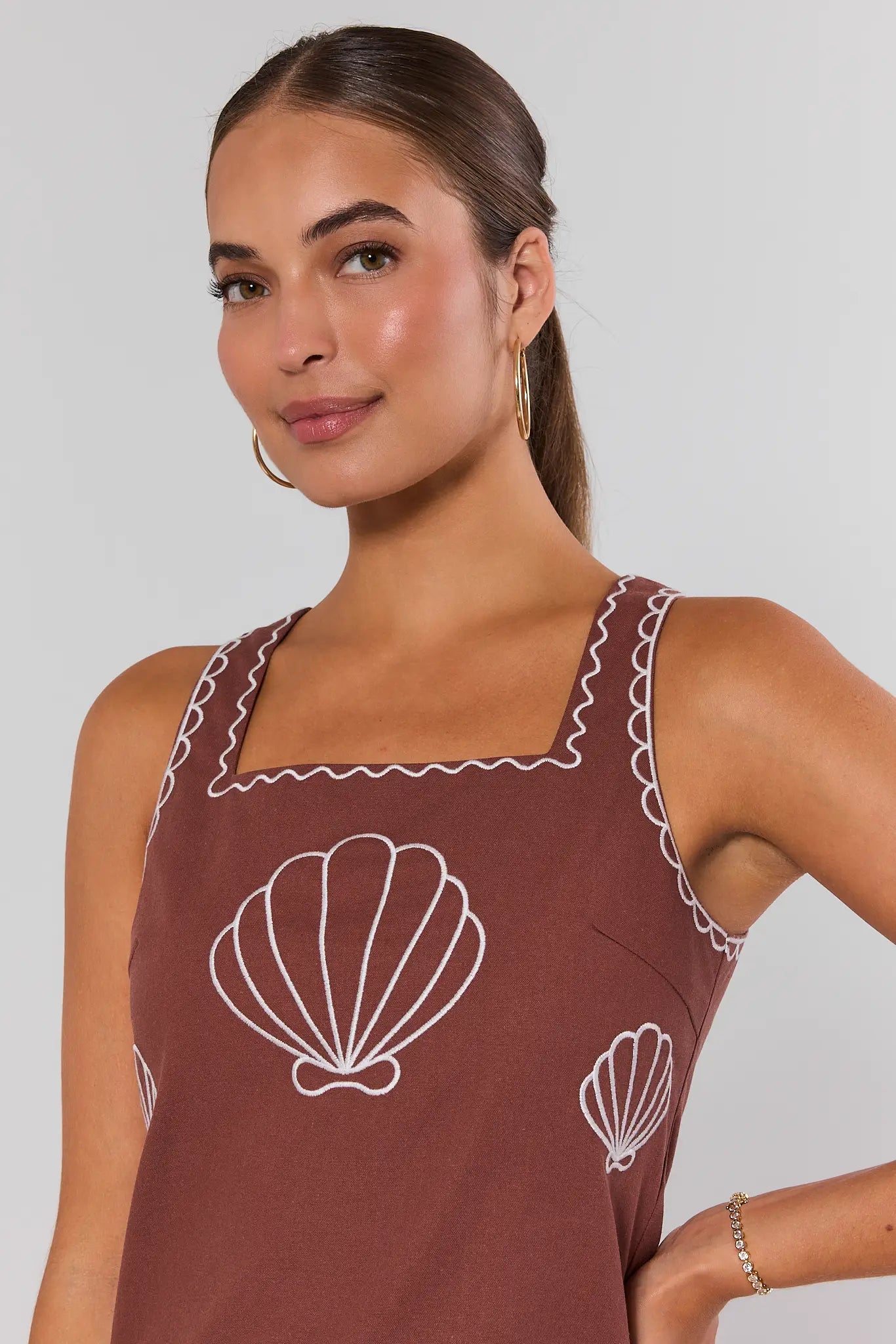 Woman wearing a brown apron with white shell patterns on a plain background close up