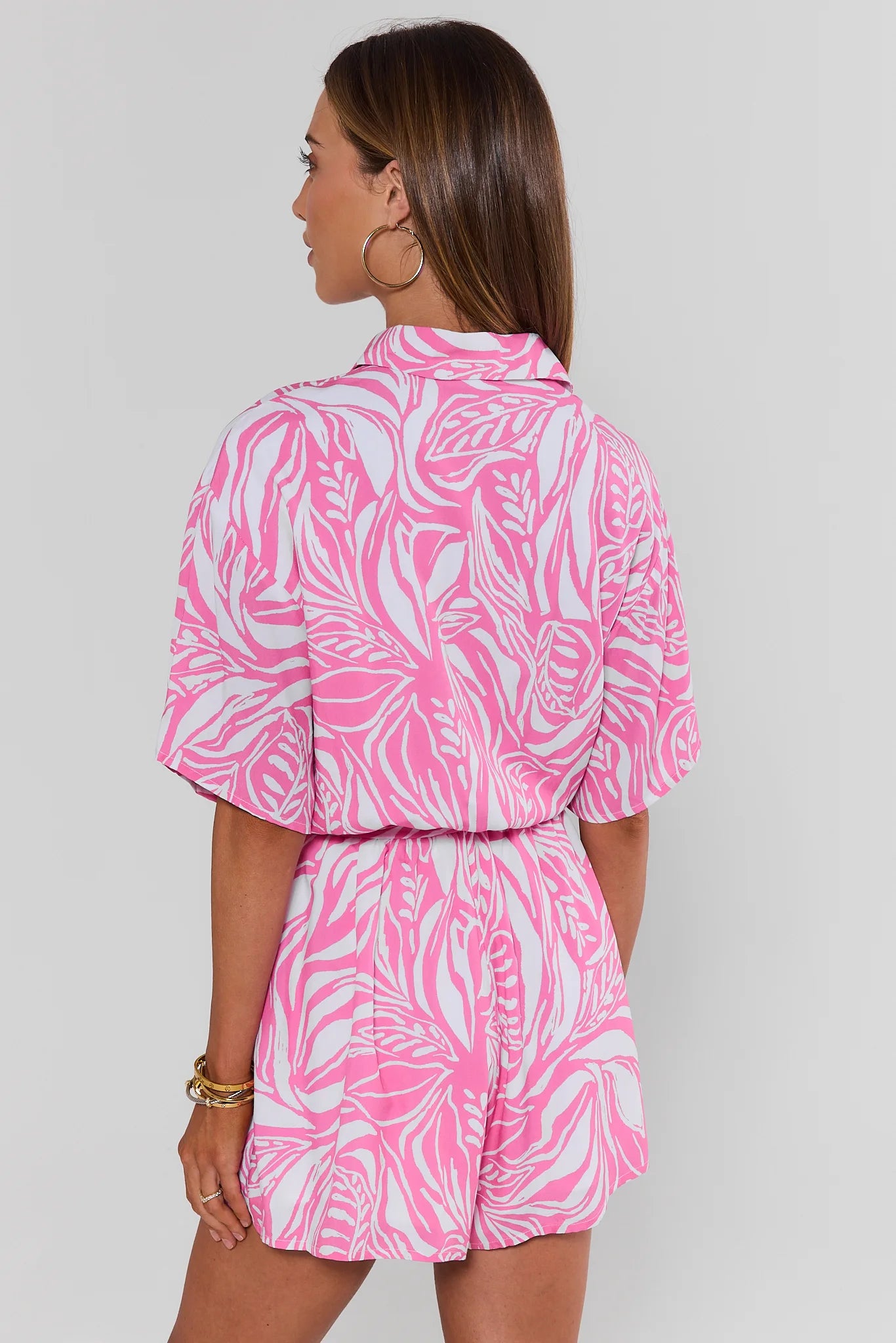 Woman standing wearing a pink and white patterned romper on a plain background