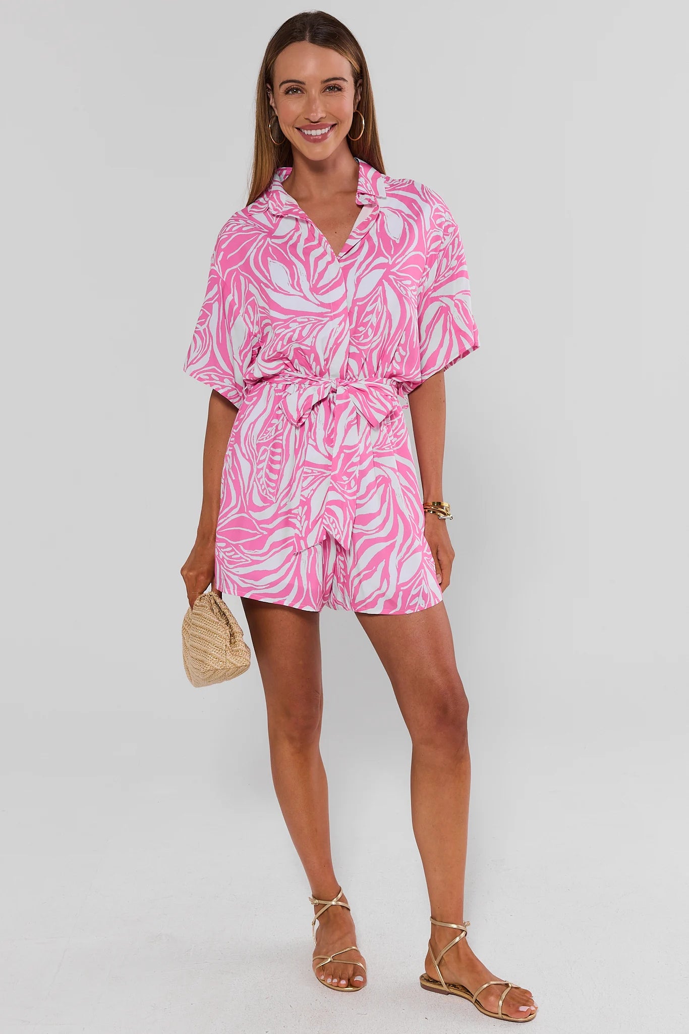 Woman wearing a pink and white patterned romper on a plain background standing
