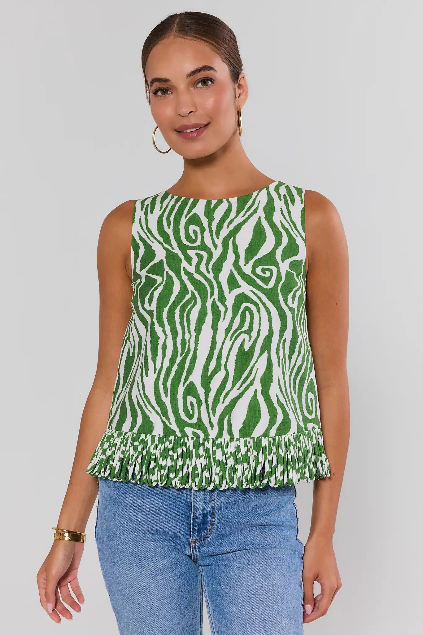 Woman wearing a green and white patterned sleeveless top with blue jeans on a plain background