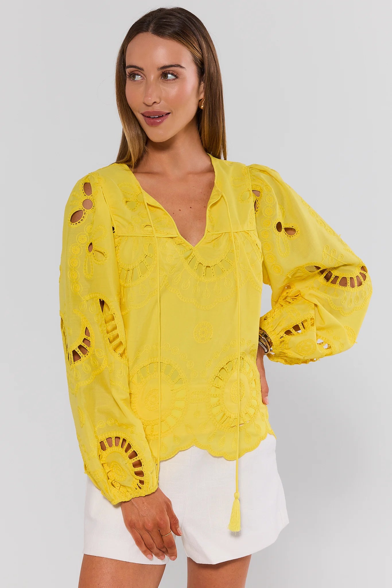Woman wearing a yellow embroidered blouse with white shorts on a light gray background