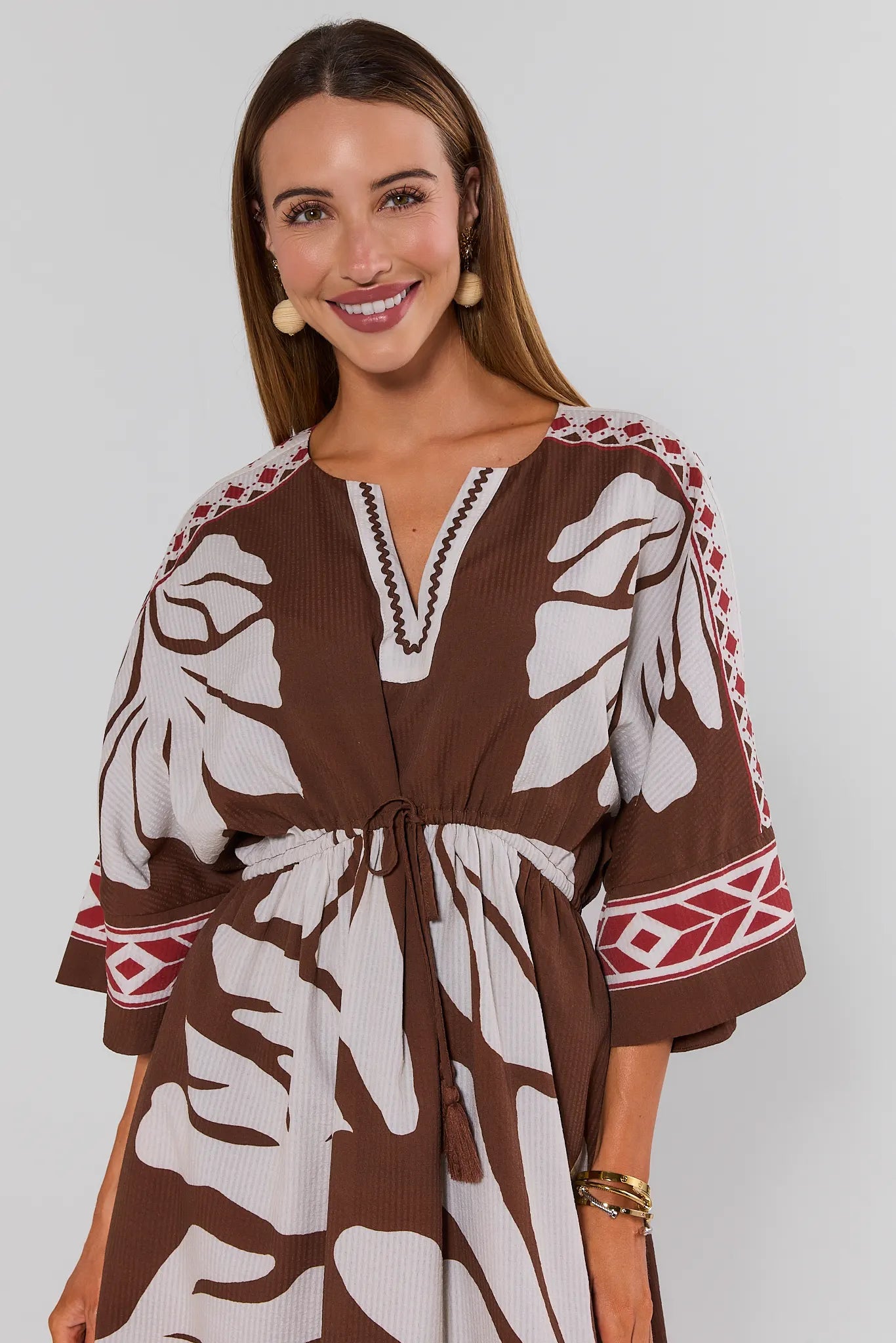 Woman wearing a brown and white patterned dress with red accents on a plain background close up