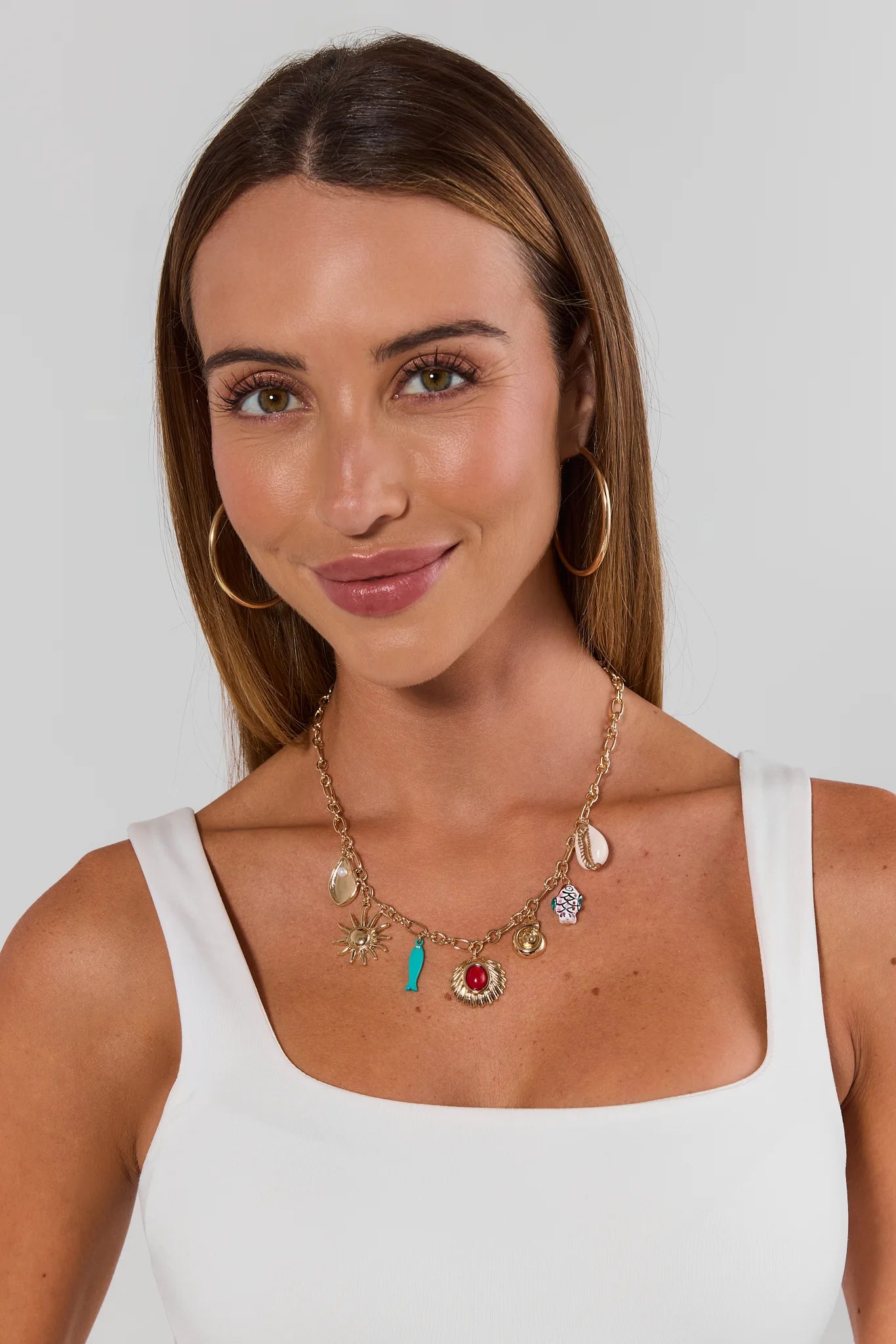 Woman wearing a necklace with various charms on a plain background