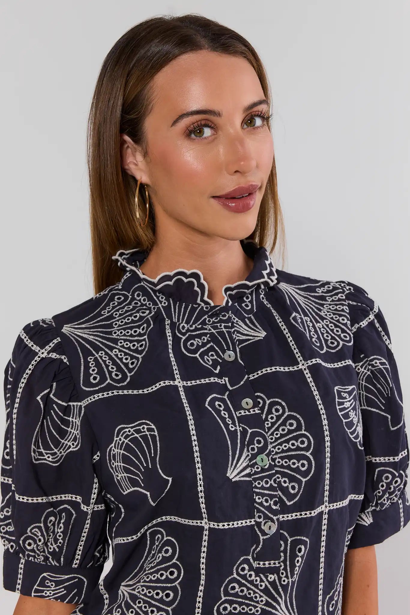 Woman wearing a navy blue blouse with white floral patterns on a plain background close up