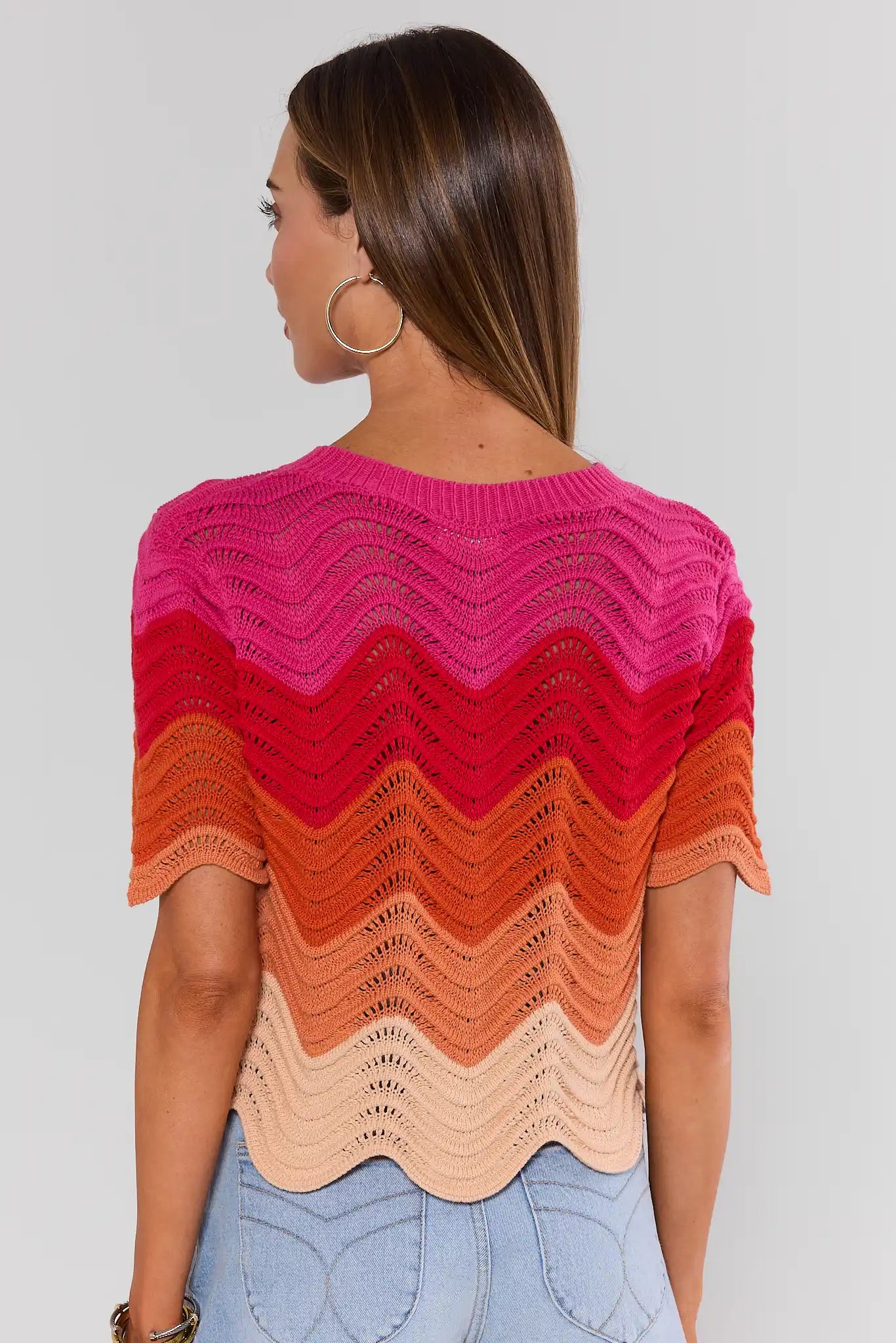 Woman wearing a colorful, patterned sweater against a plain background standing