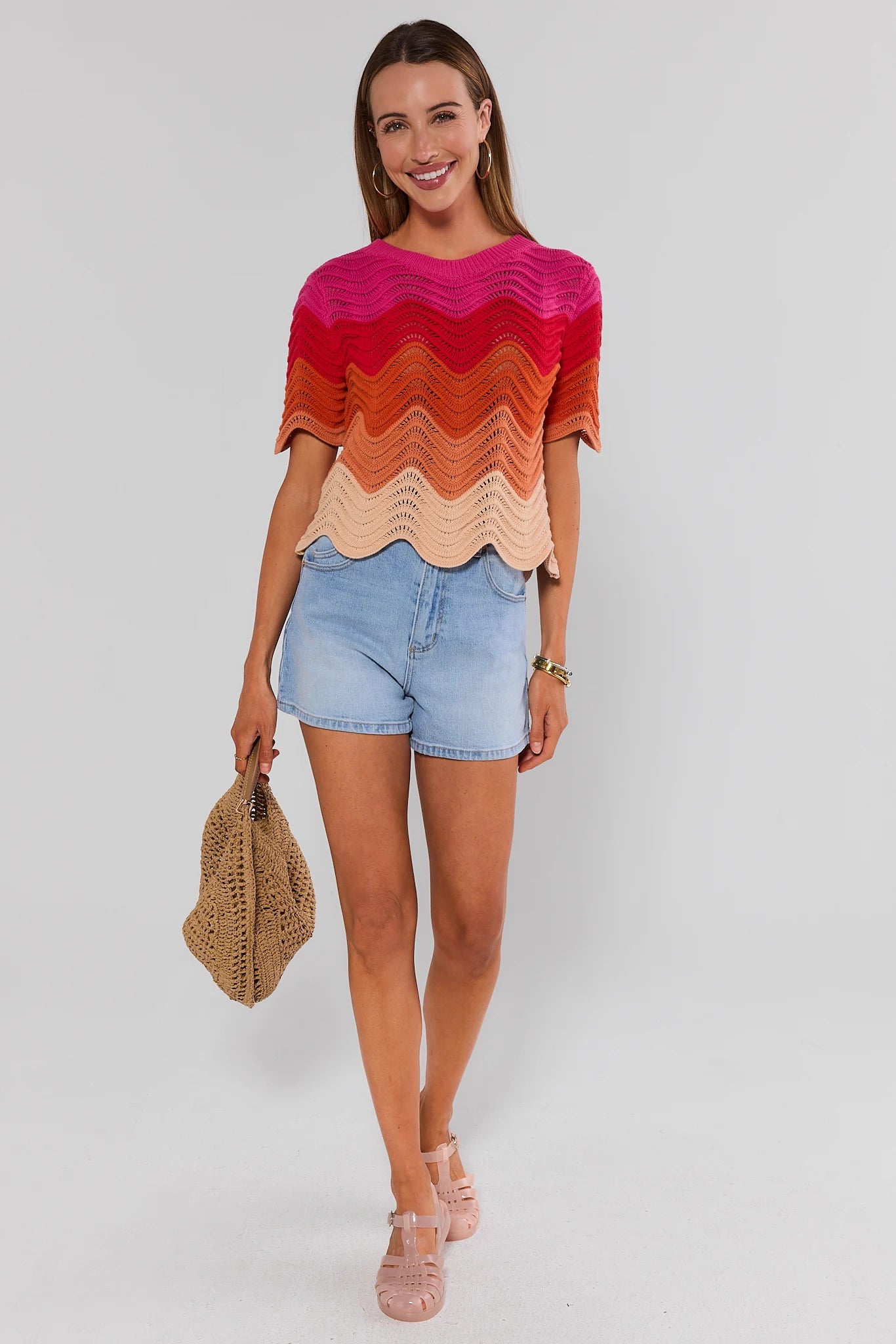 Woman wearing a colorful striped sweater and denim shorts on a plain background