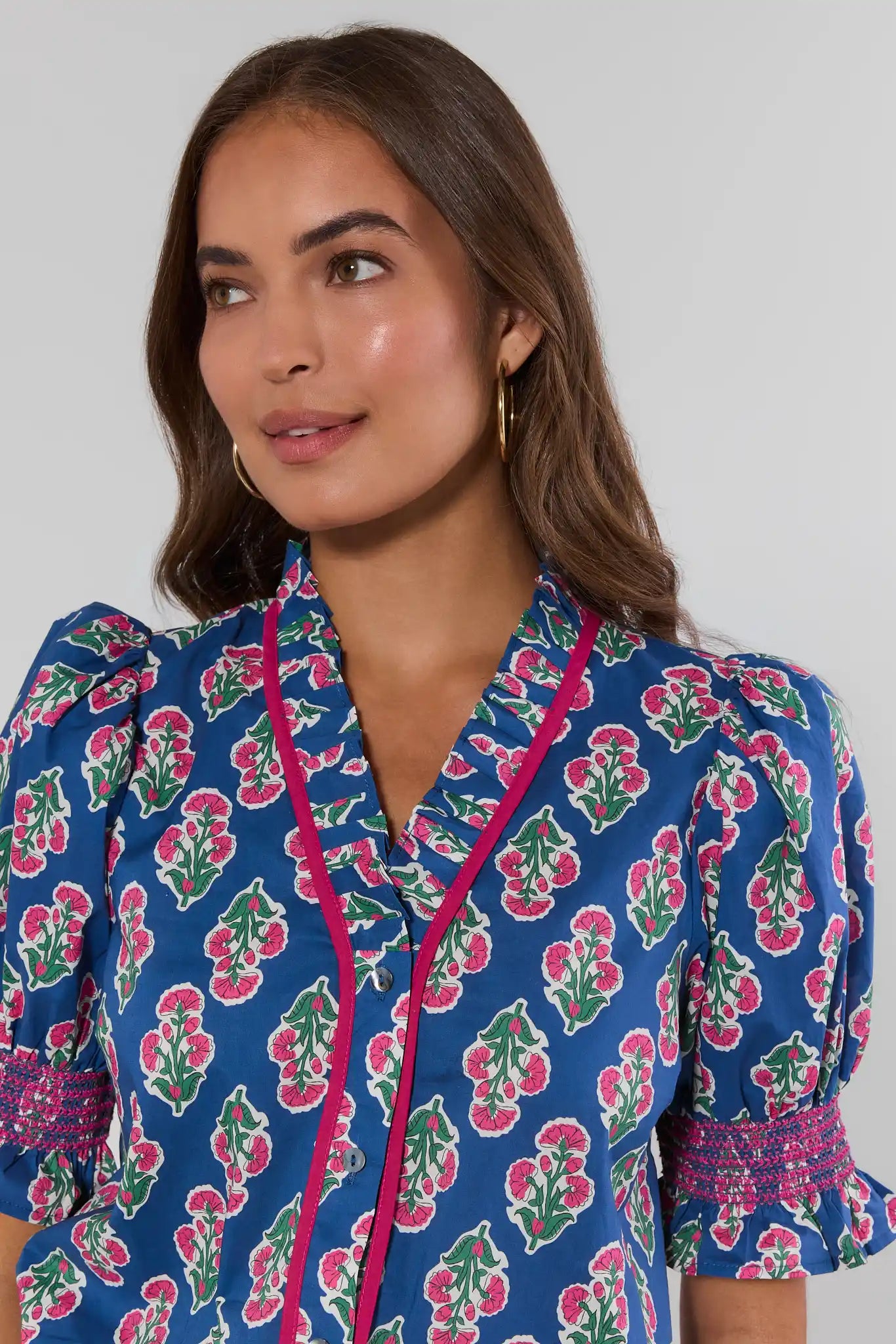 Woman wearing a blue floral dress with pink accents against a plain background close up