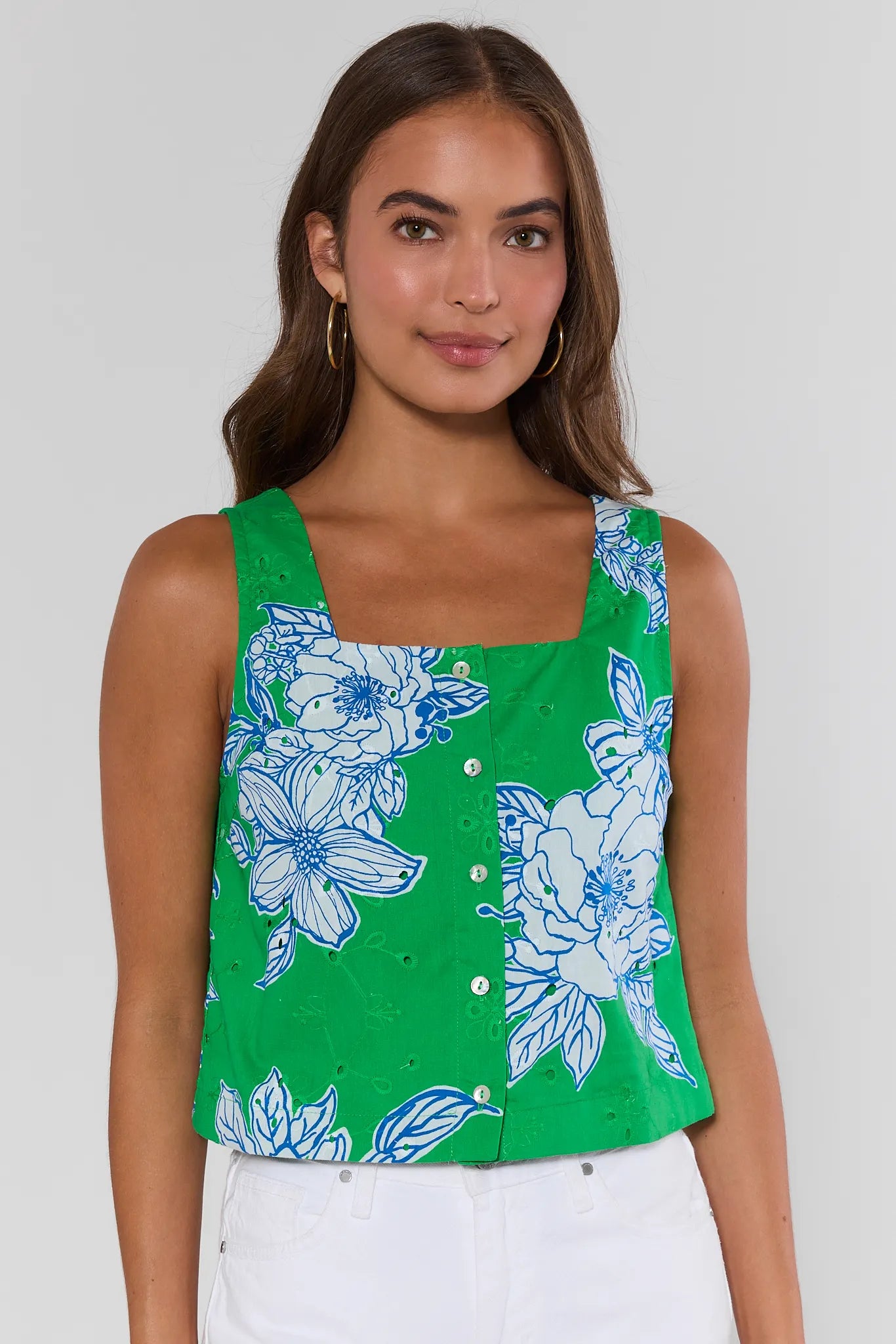 Woman wearing a green sleeveless top with blue floral pattern on a white background standing