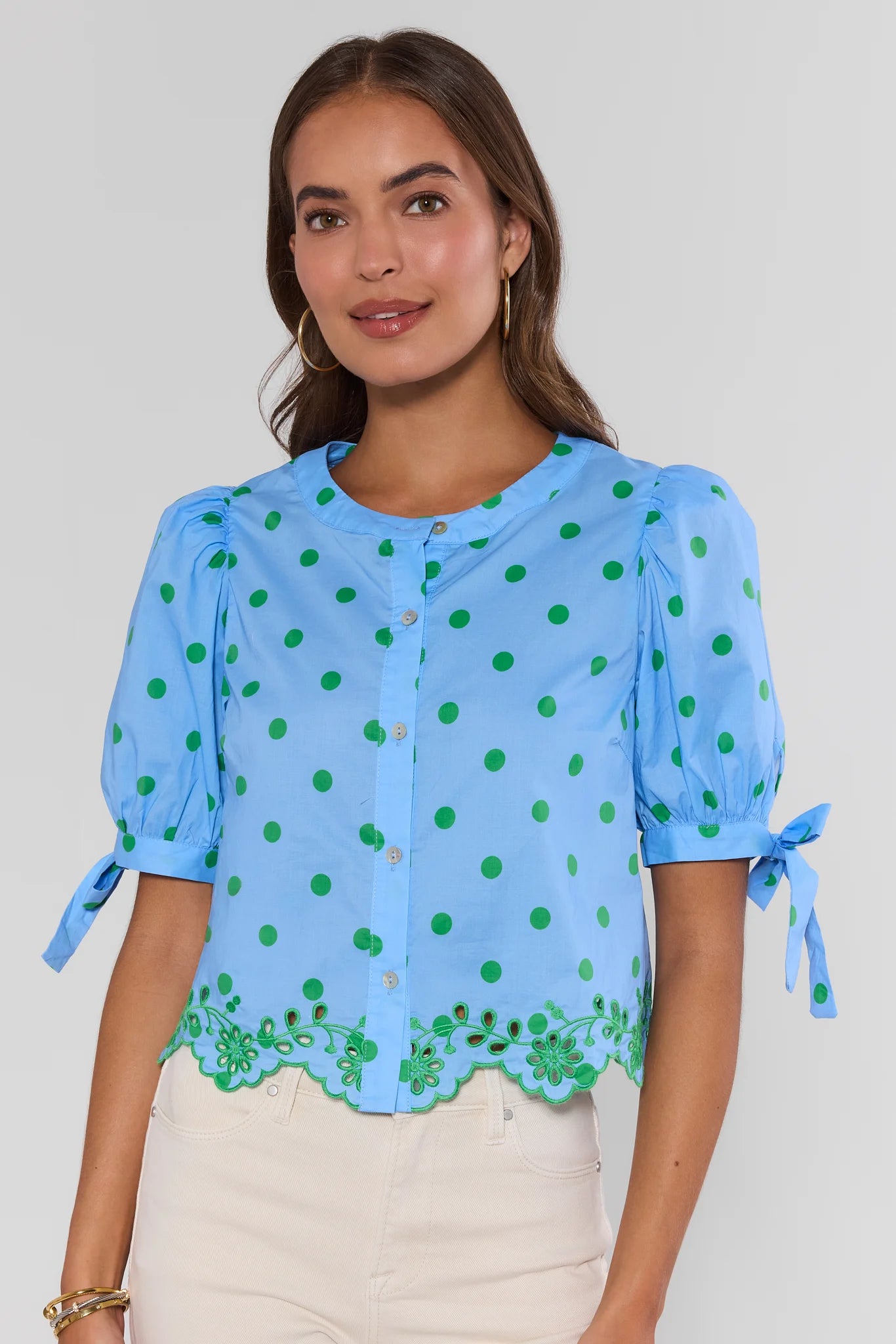 Woman wearing a blue blouse with green polka dots and tied sleeves on a plain background standing