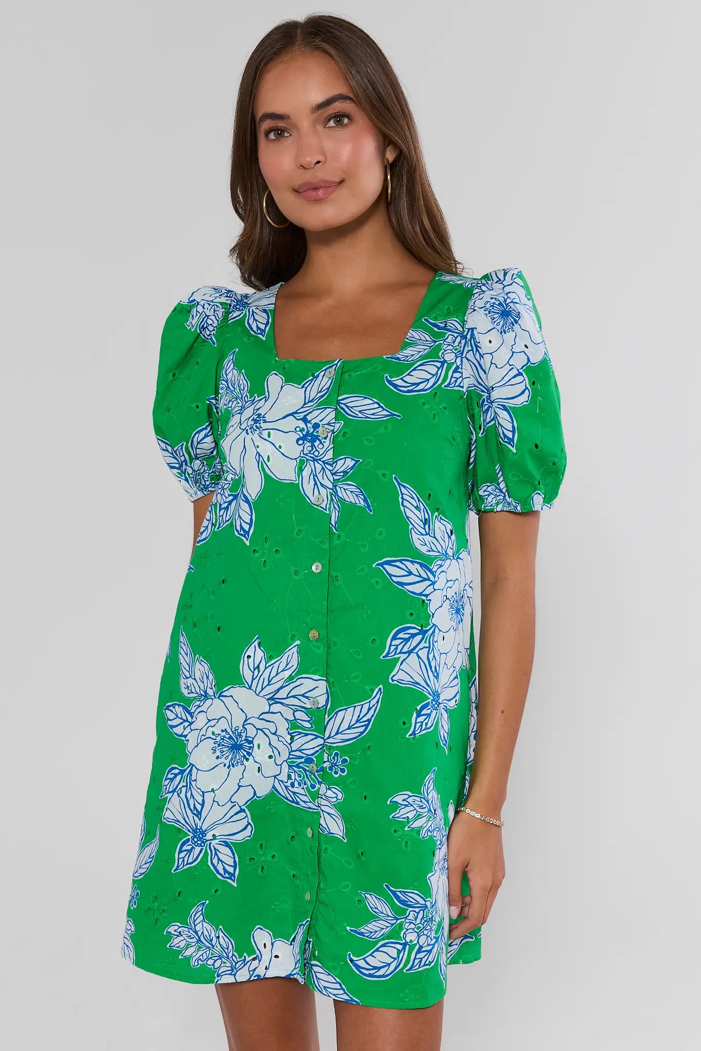 Woman wearing a green dress with blue floral pattern on a white background standing