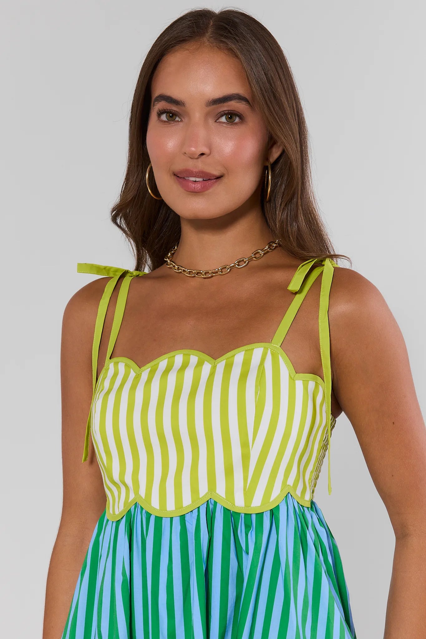 Woman wearing a green and white striped top with a blue and green striped skirt against a plain background close up