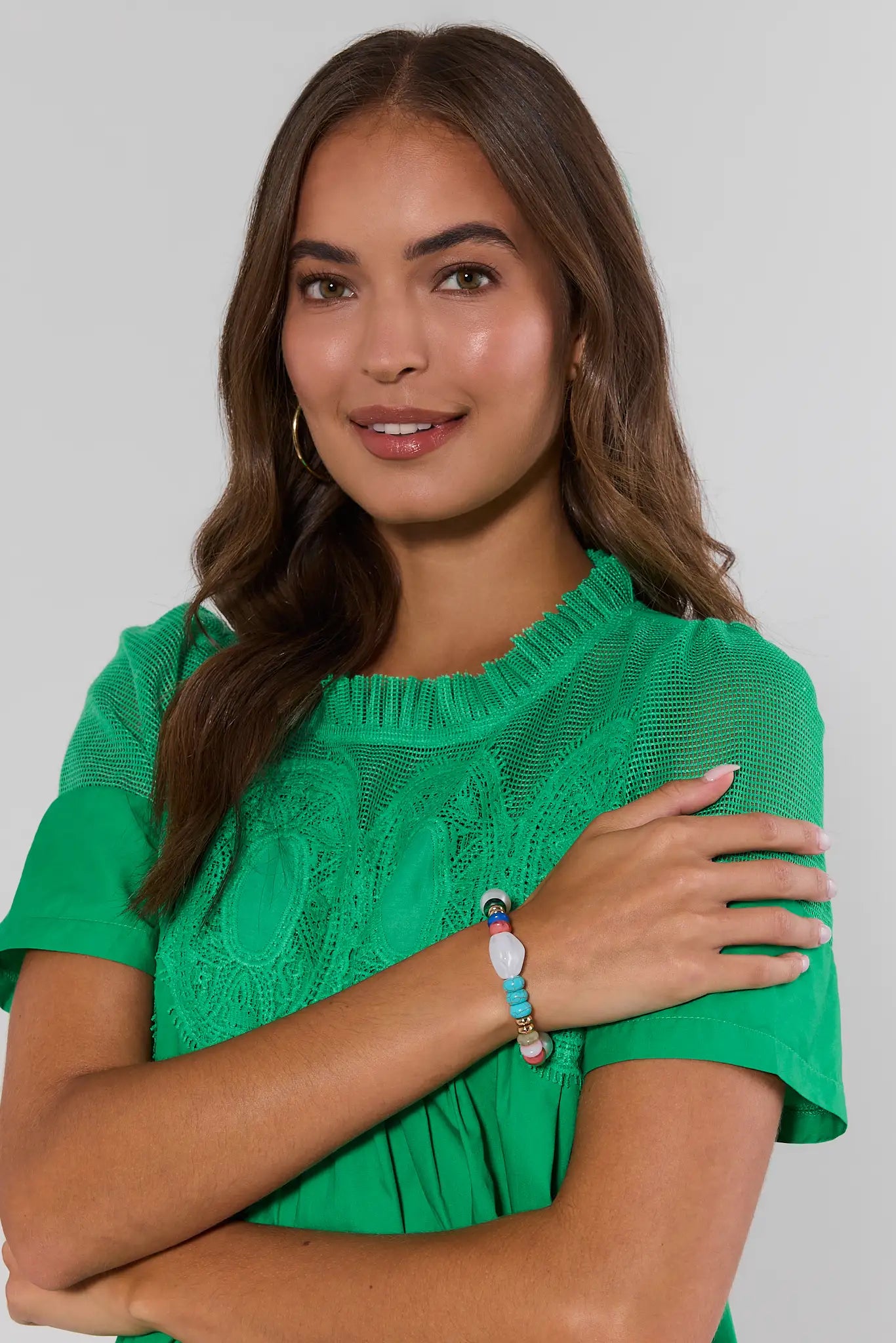 Woman wearing a green top and colorful bracelet with a plain background