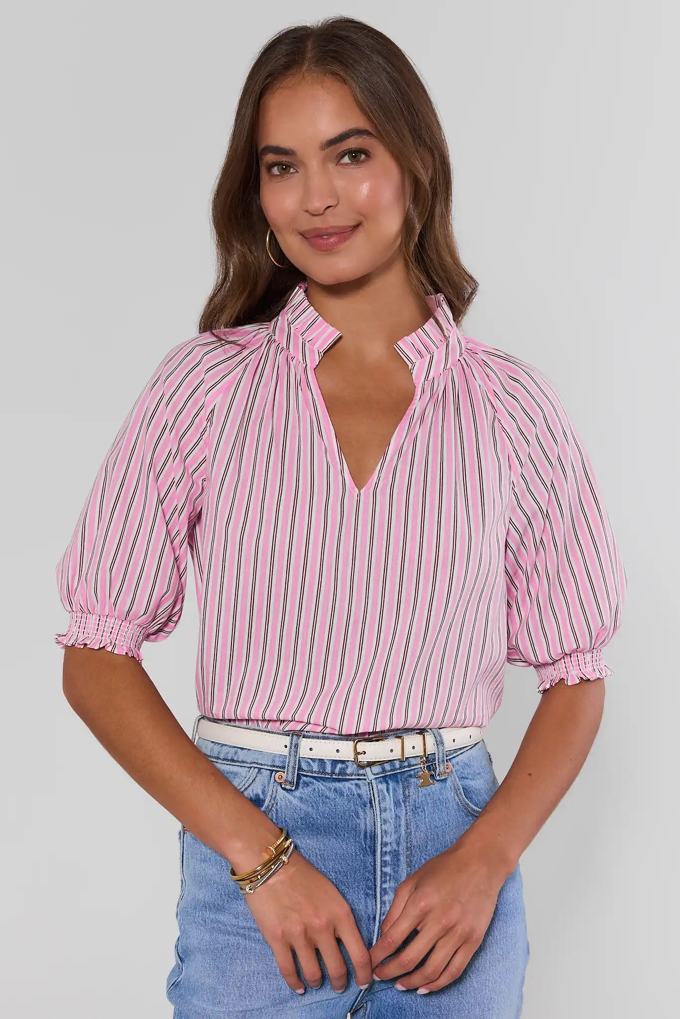 Woman wearing a pink and white striped blouse with blue jeans on a plain background