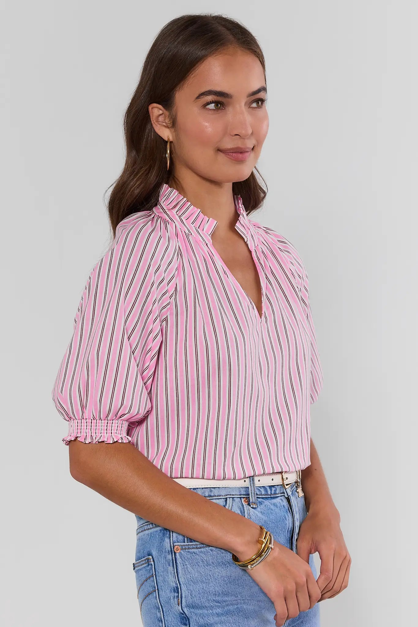 Woman wearing a pink and white striped blouse with blue jeans on a plain background side