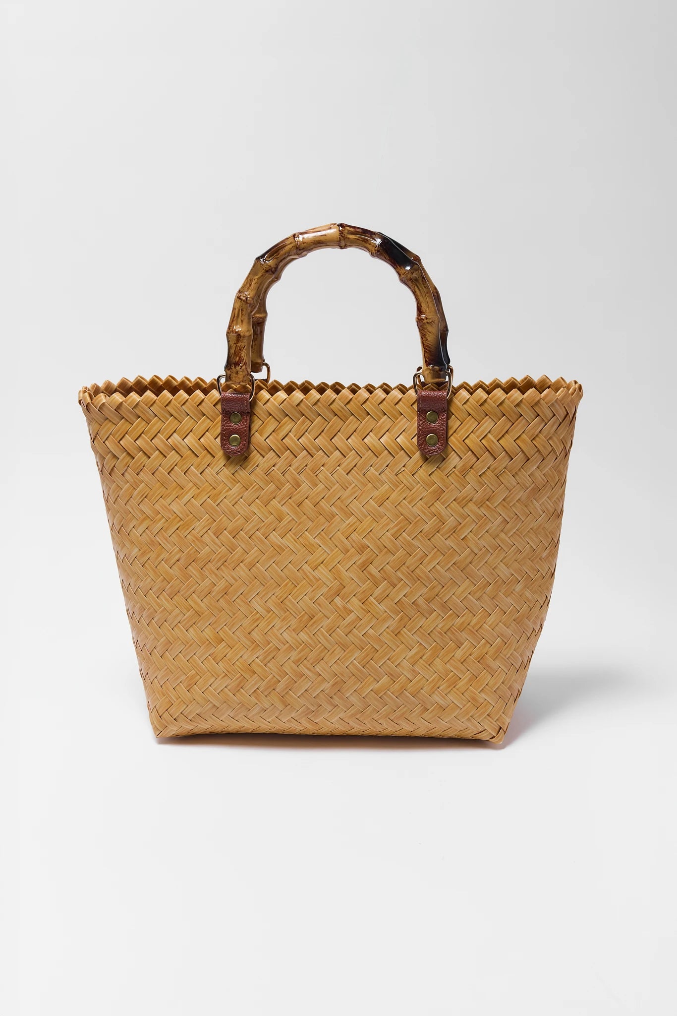 Woven straw tote bag with brown handles on a white background