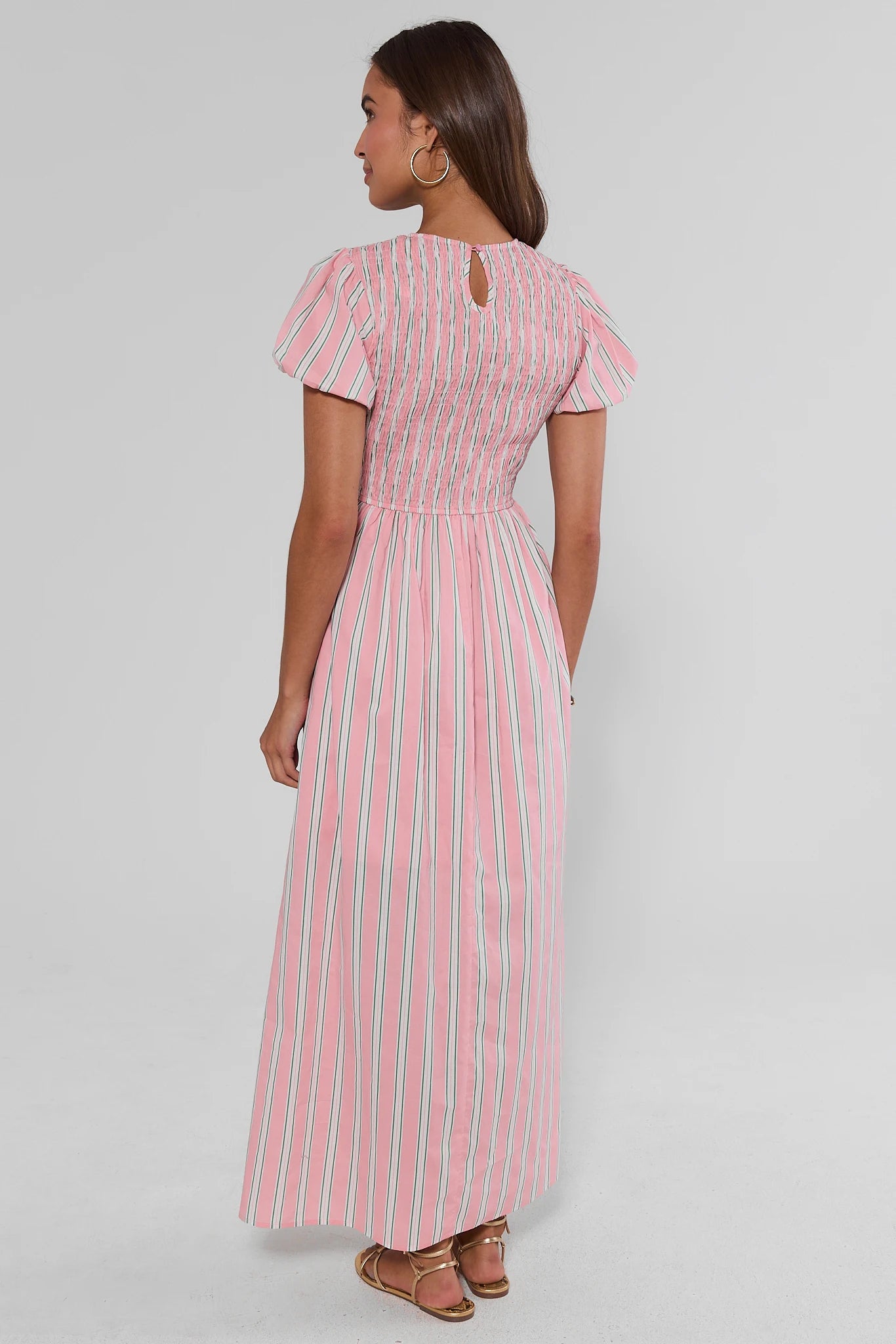 Woman wearing a pink and white striped dress on a plain background walking