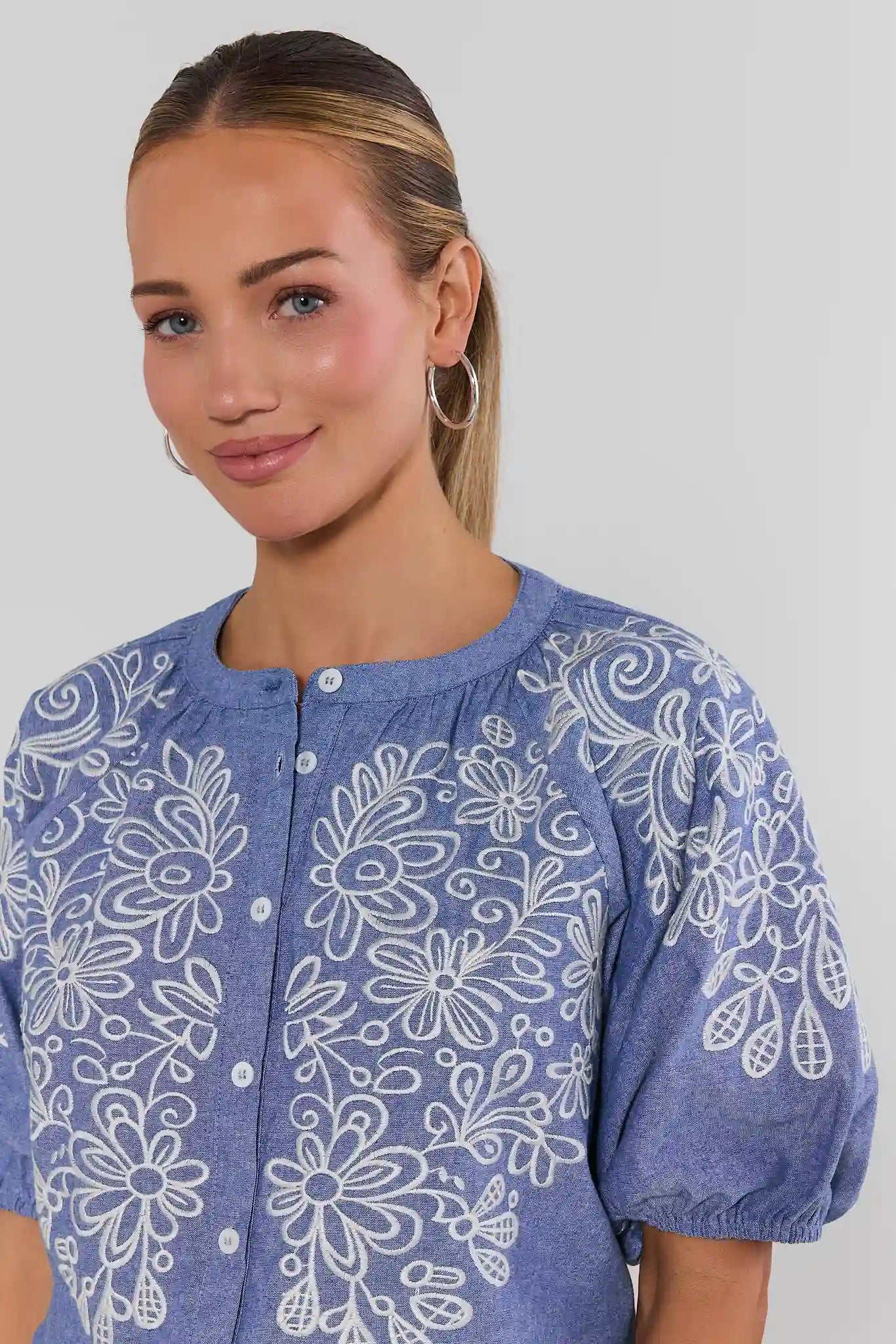 Woman wearing a blue floral patterned blouse against a plain background close up